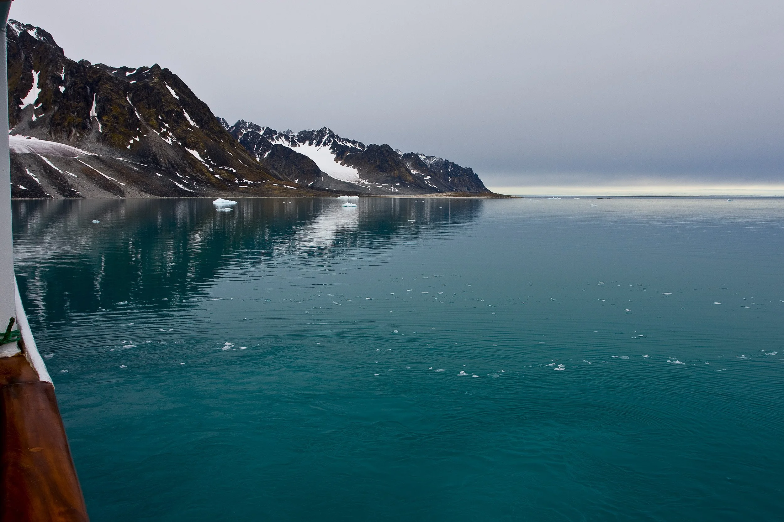 Turquoise water and scattered ice drift past the ship in Magdalenefjorden under a low Arctic sky.