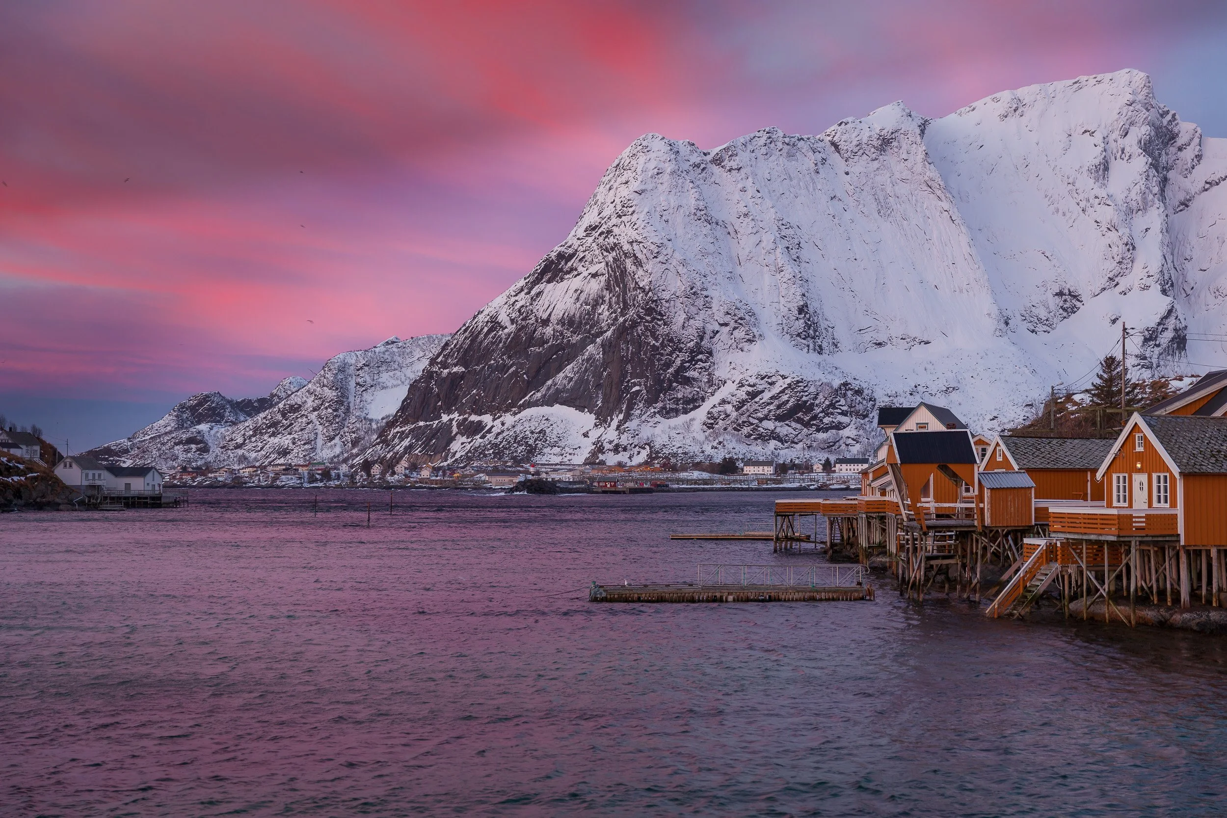 Sunrise in Reine, Lofoten Islands, Norway – golden light on red cabins, calm water and sharp mountain silhouettes.