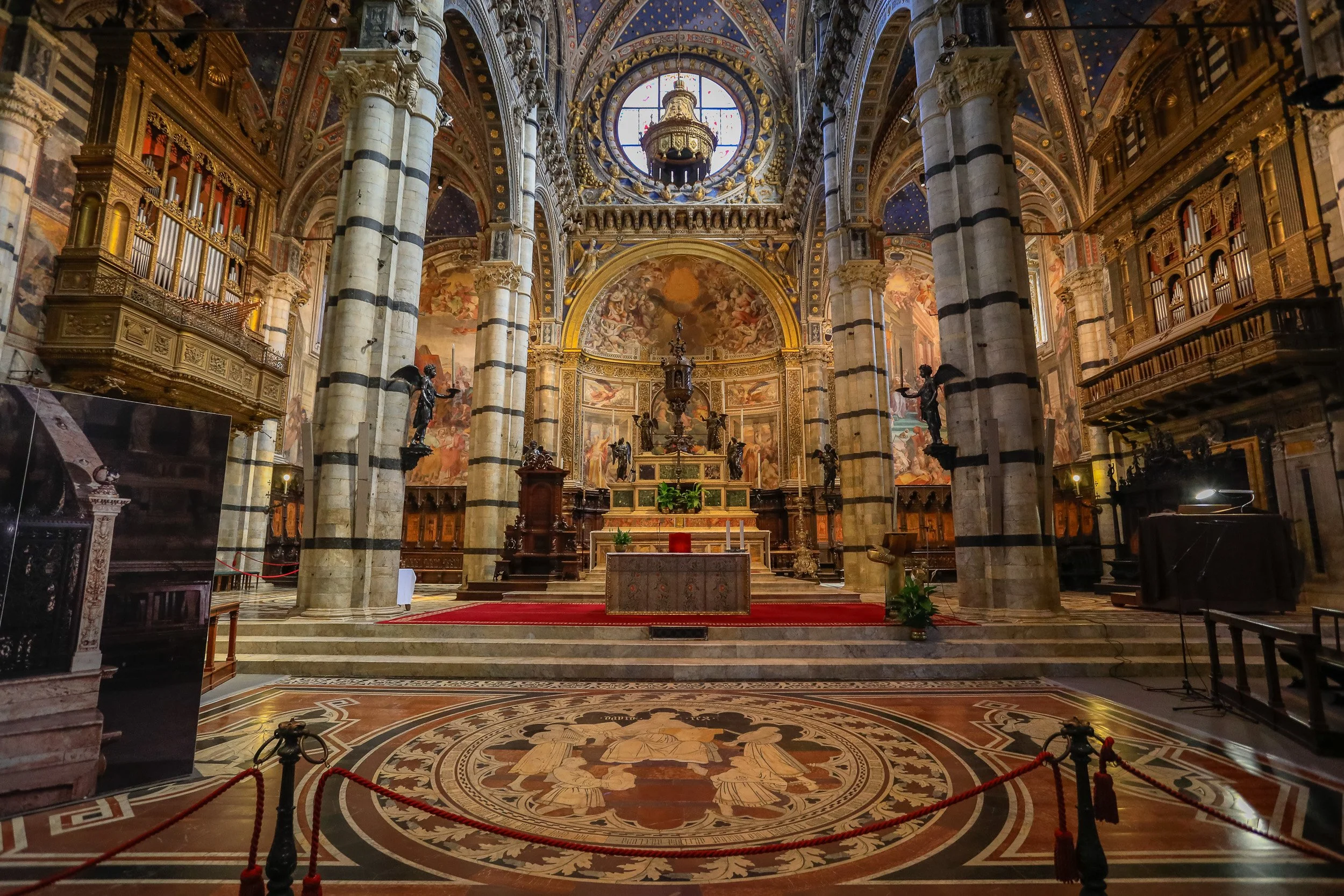 The richly patterned interior of Siena Cathedral, where striped columns, frescoes and polished stone lead towards the altar.