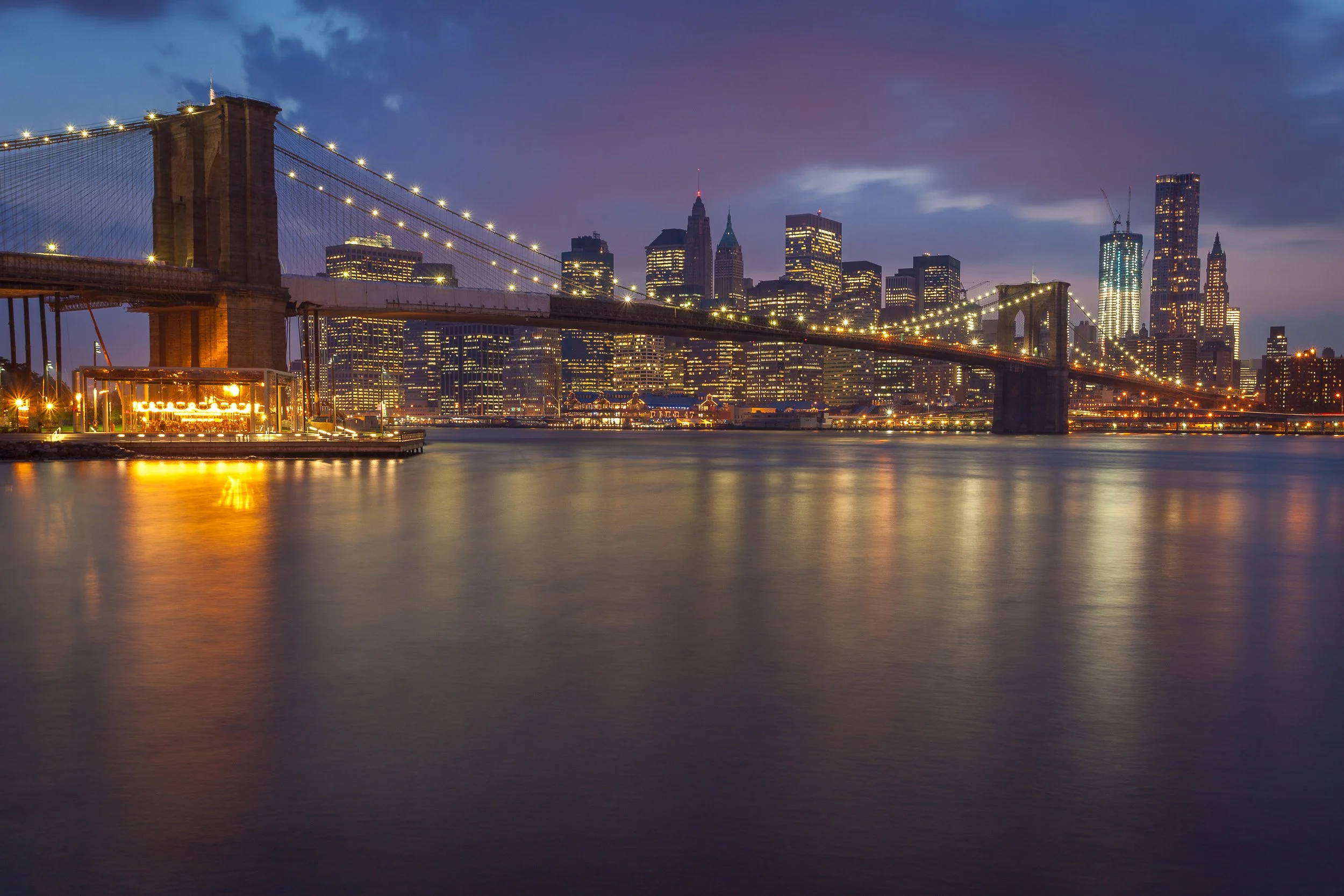 Brooklyn Bridge at blue hour, its lights leading the eye towards Manhattan’s glowing skyline.
