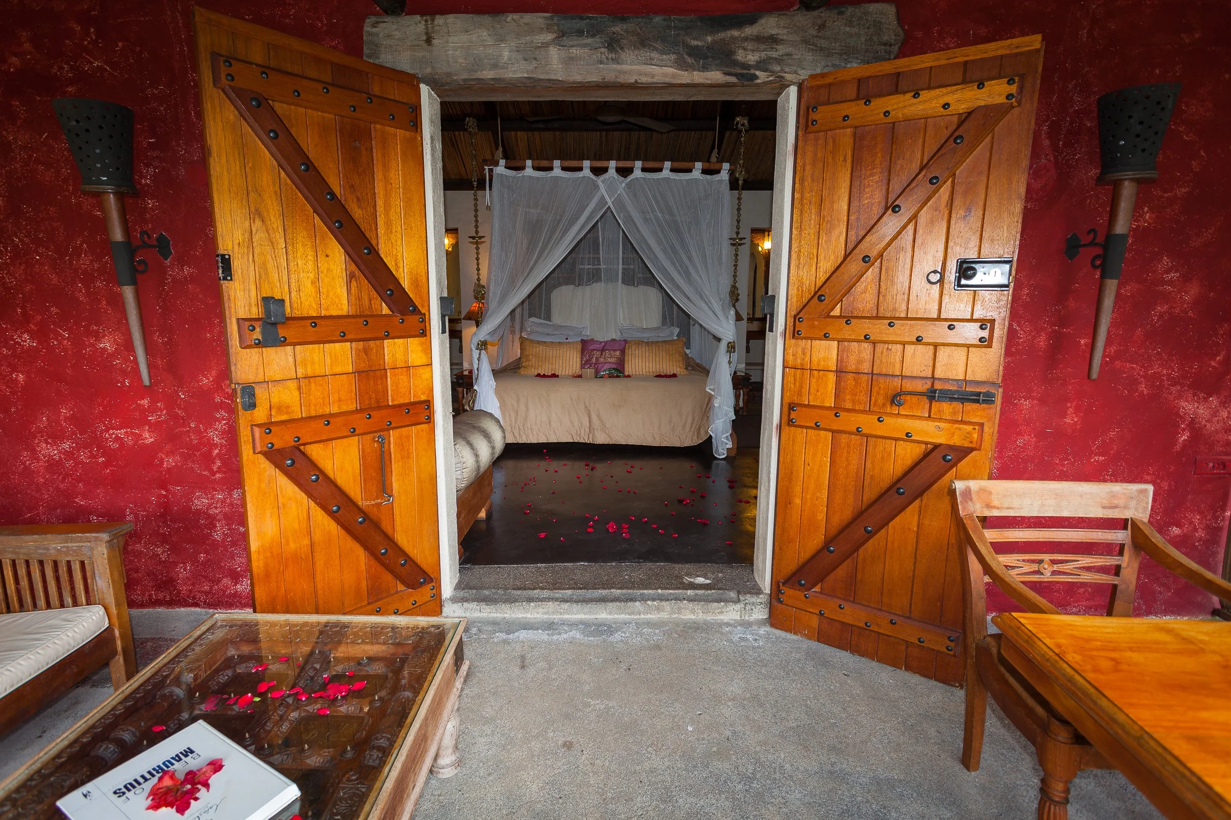 Cosy suite at Lakaz Chamarel in the Mauritian mountains, with a four-poster bed, wooden doors and rose petals scattered across the floor