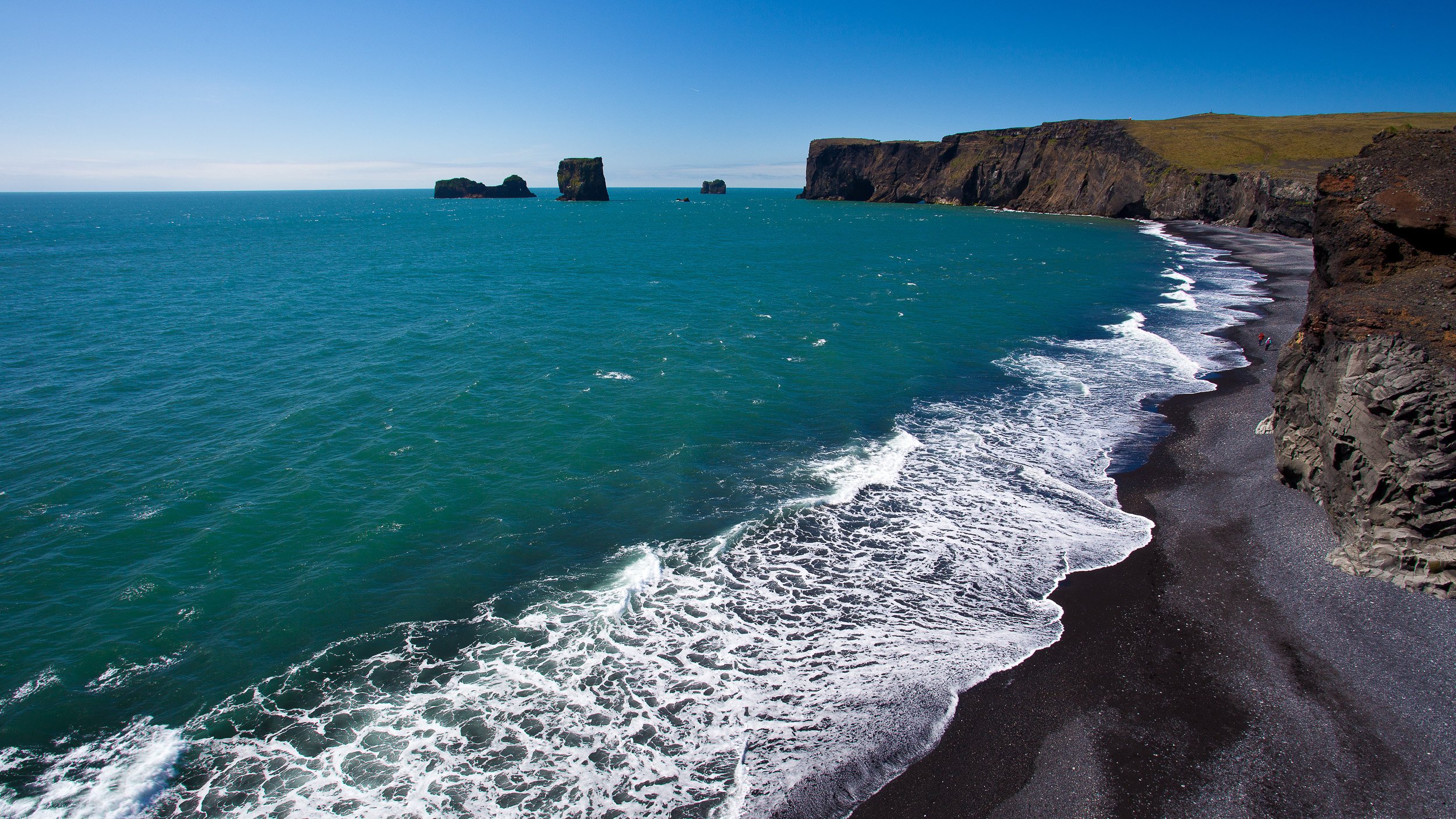 Dyrhólaey on the south coast of Iceland, with black volcanic sand, sea stacks, dark cliffs and Atlantic waves shaping a raw coastal landscape.