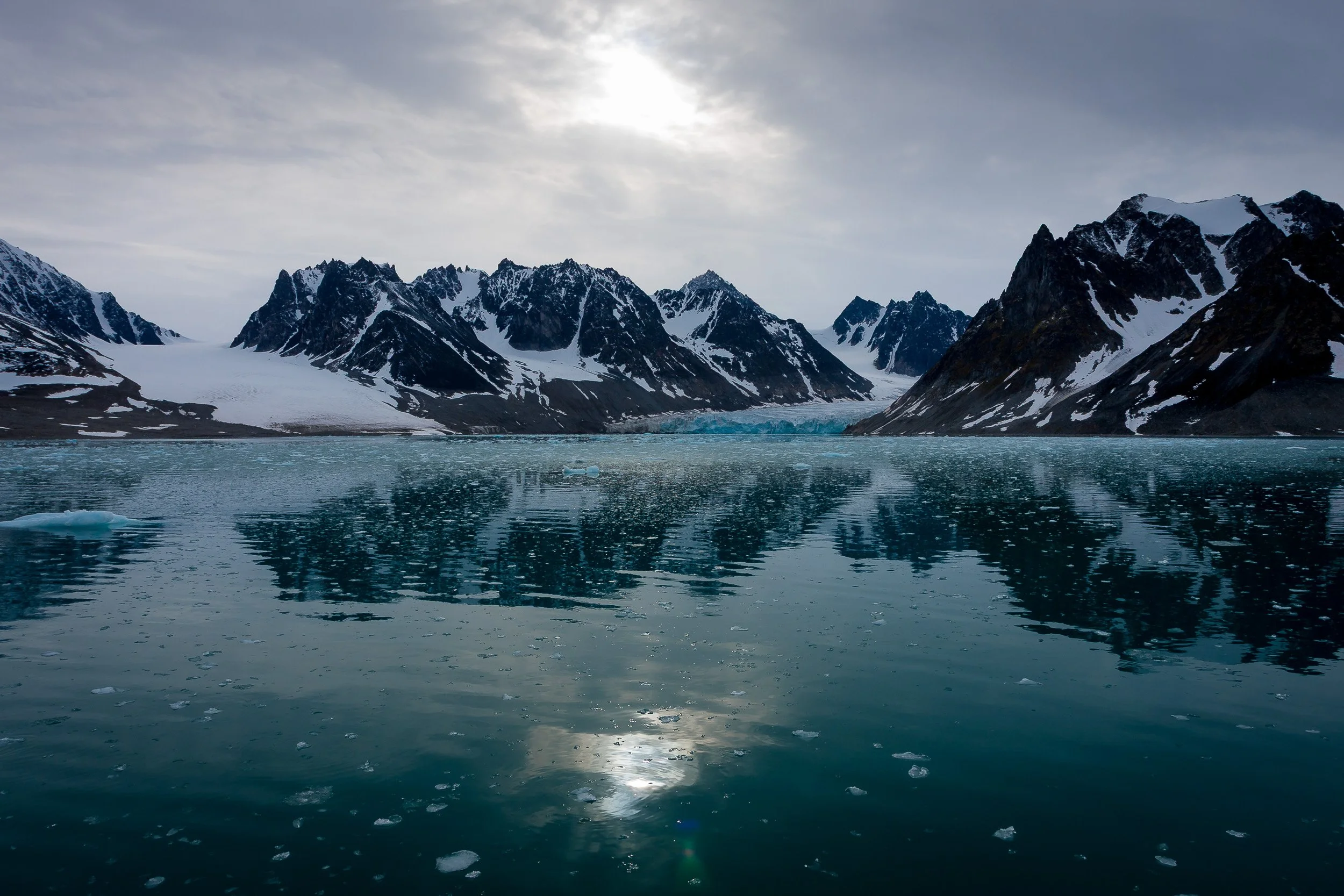 Dark peaks and glacier ice frame the still waters of Magdalenefjorden beneath a pale Arctic sun.