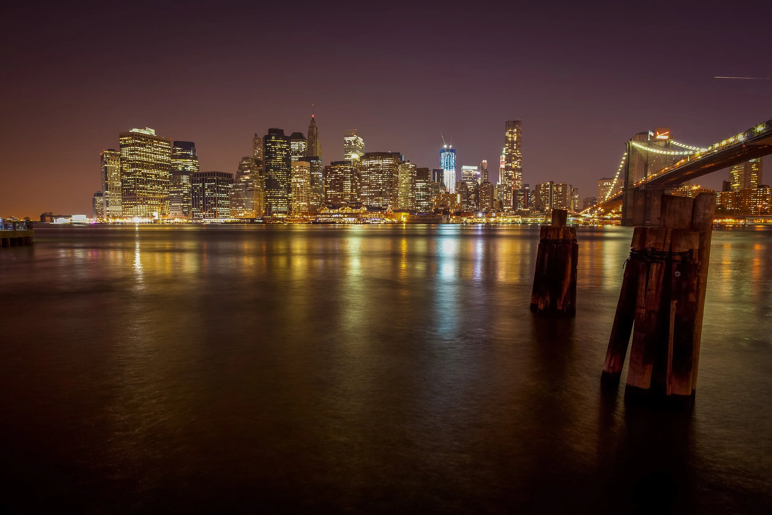 Lower Manhattan and the Brooklyn Bridge reflected in still night water.