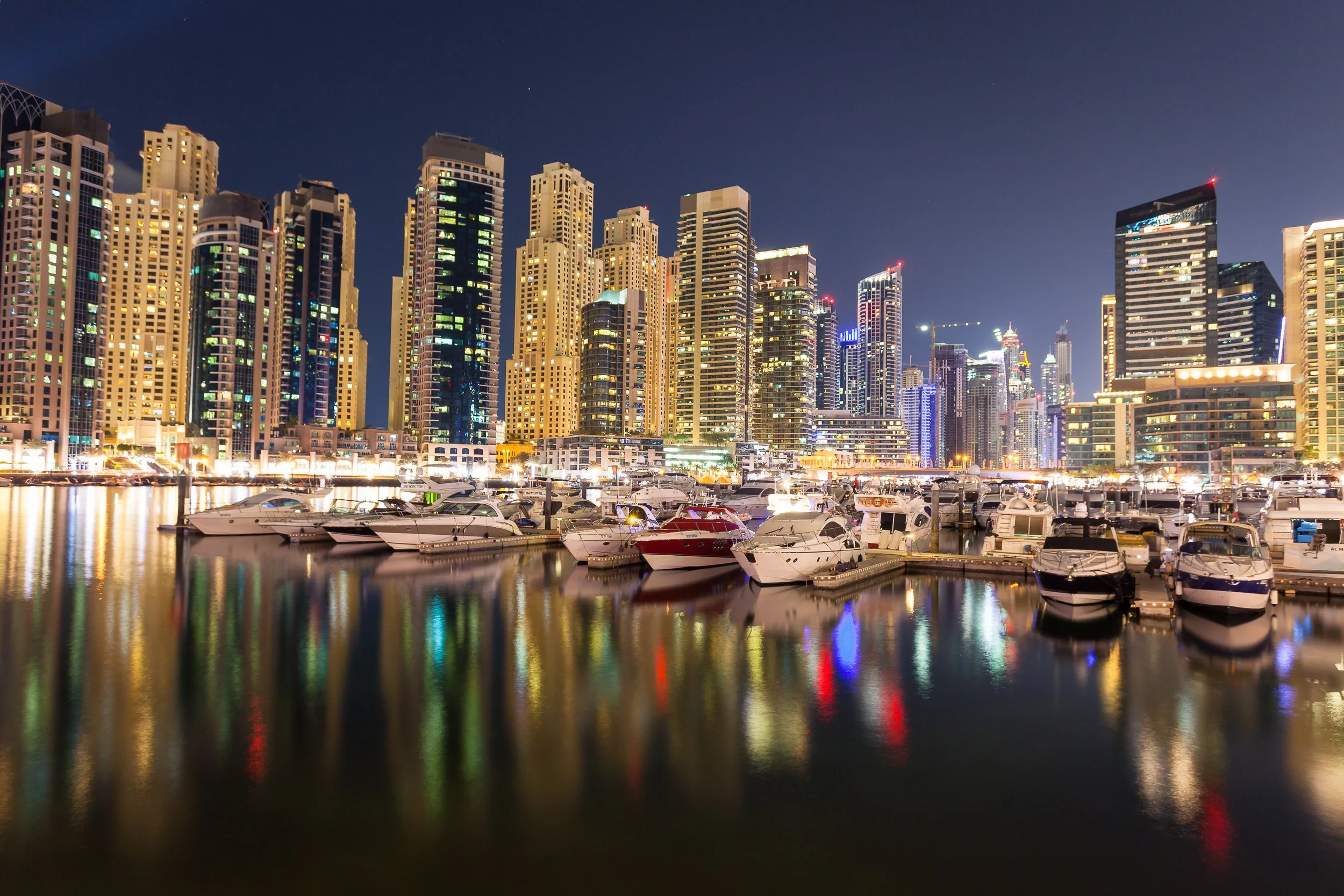 Moored yachts and mirrored lights capturing the calm glamour of Dubai Marina at night.