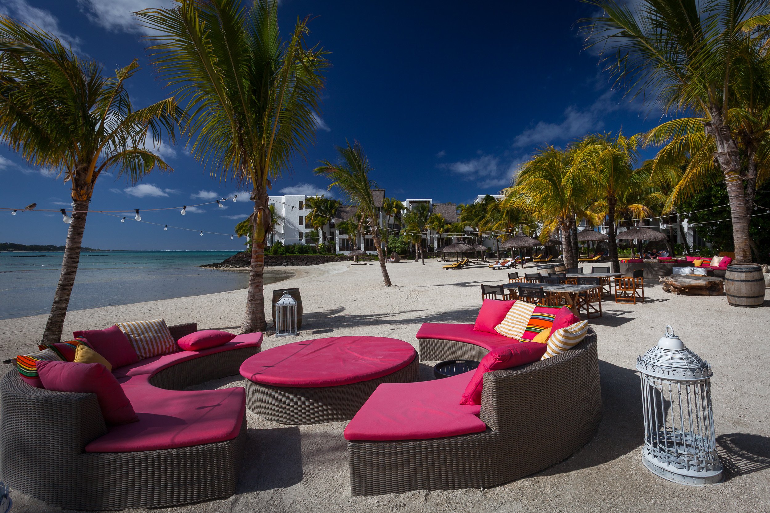 Bright pink lounge sofas set under palm trees on the beach at Shangri-La’s Le Touessrok Resort, perfect for soaking up Mauritian luxury.