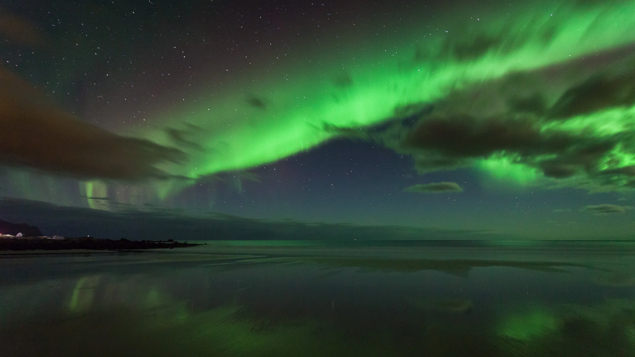 Northern Lights at Skagsanden Beach in Flakstad, Lofoten, Norway – aurora reflected in wet sand and Arctic waves.