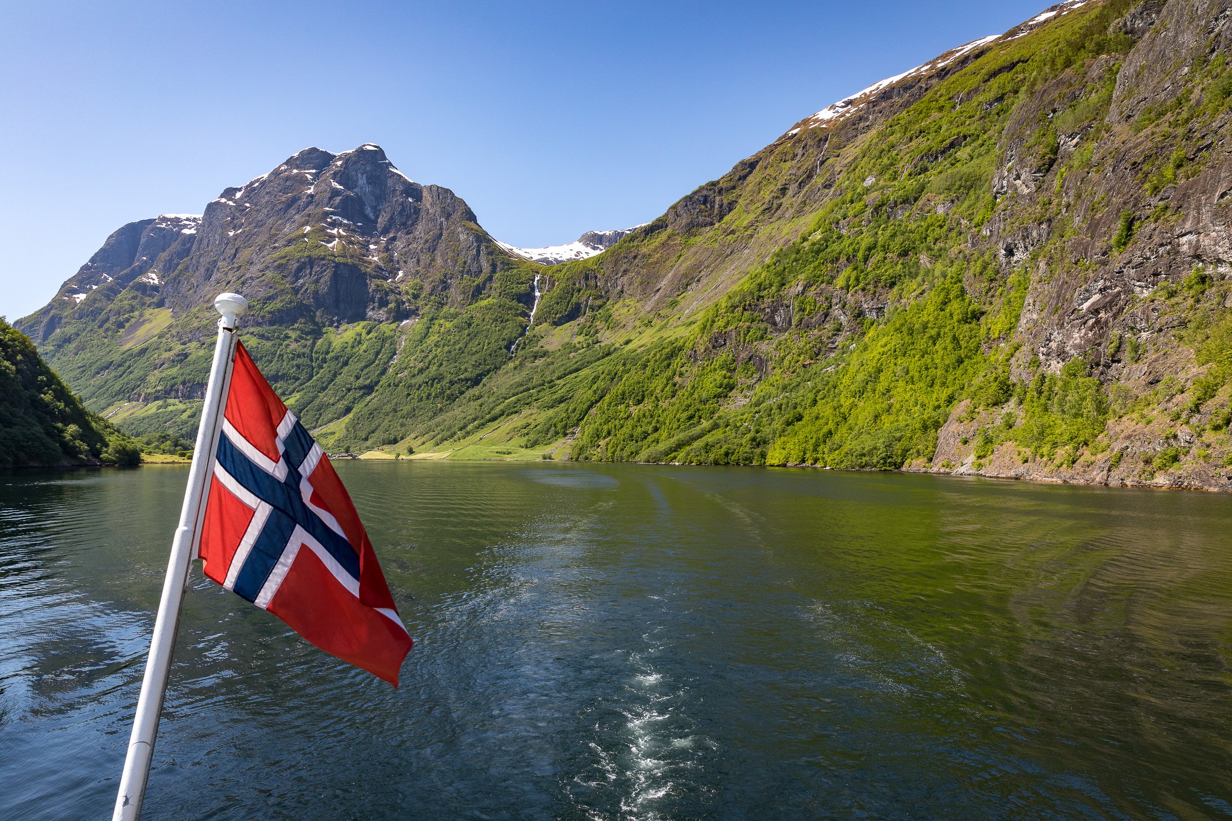 Hardangerfjorden at speed — a boat cuts across calm water, leaving a bright signature on Norway’s deep fjord blue.