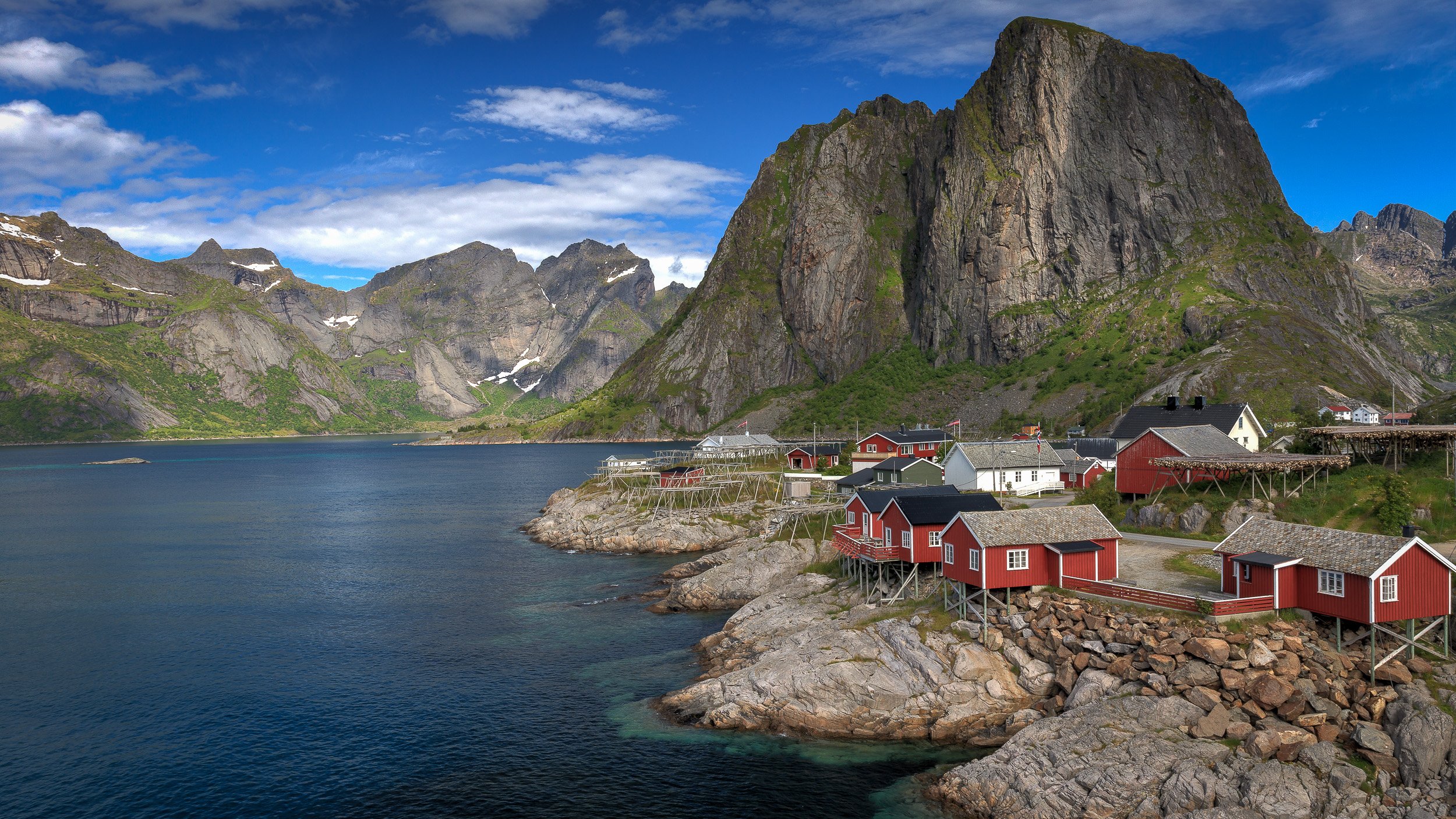 Hamnøy in the Lofoten Islands, Norway – red fisherman’s cabins stand on rocky islets beneath towering cliffs, connected by a narrow bridge. The mix of rugged rock, traditional buildings and sweeping mountains makes this a classic, often-photographed 