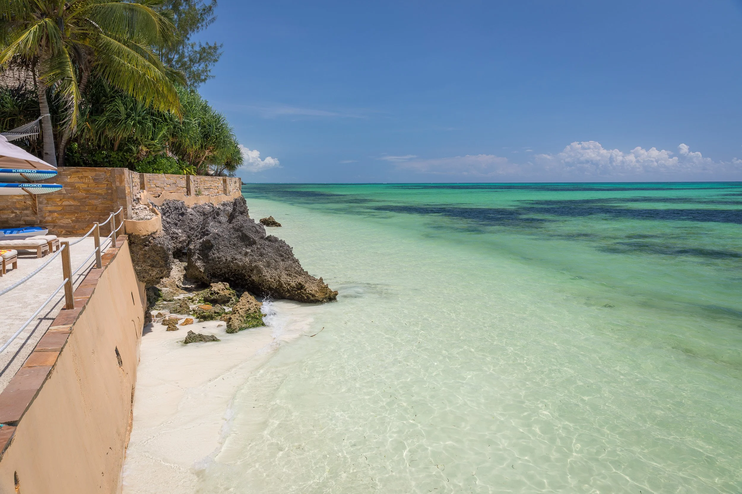 Beachfront at Tulia Zanzibar Unique Beach Resort – curved shoreline, reef-protected lagoon and palm trees reaching towards the Indian Ocean.