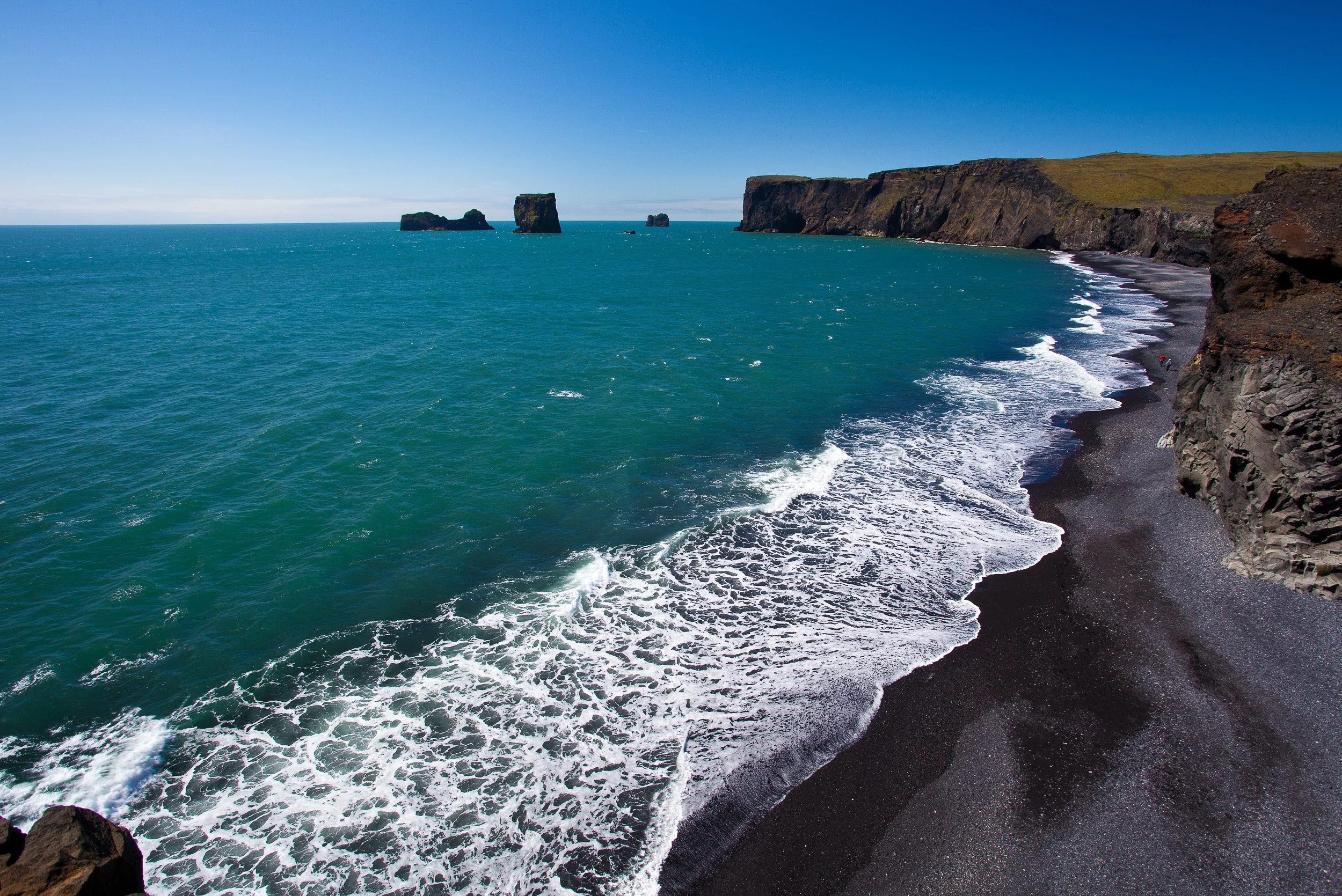 Dyrholaey’s sweeping headland leads the eye along a black-sand curve of surf, out towards isolated sea stacks under clear, wind-bright Atlantic light.