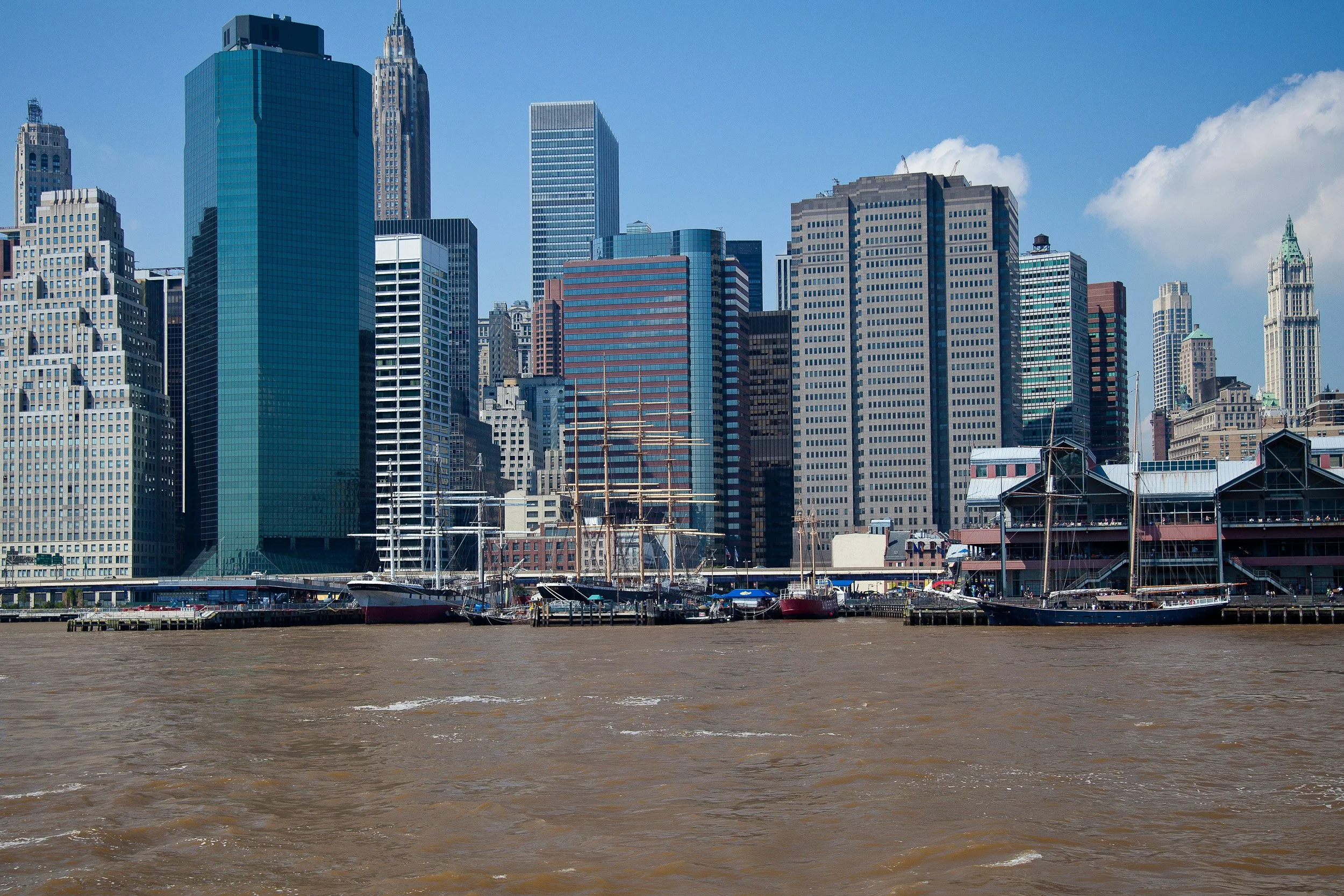 Downtown Manhattan seen from the water, where piers, masts and towers line the waterfront.