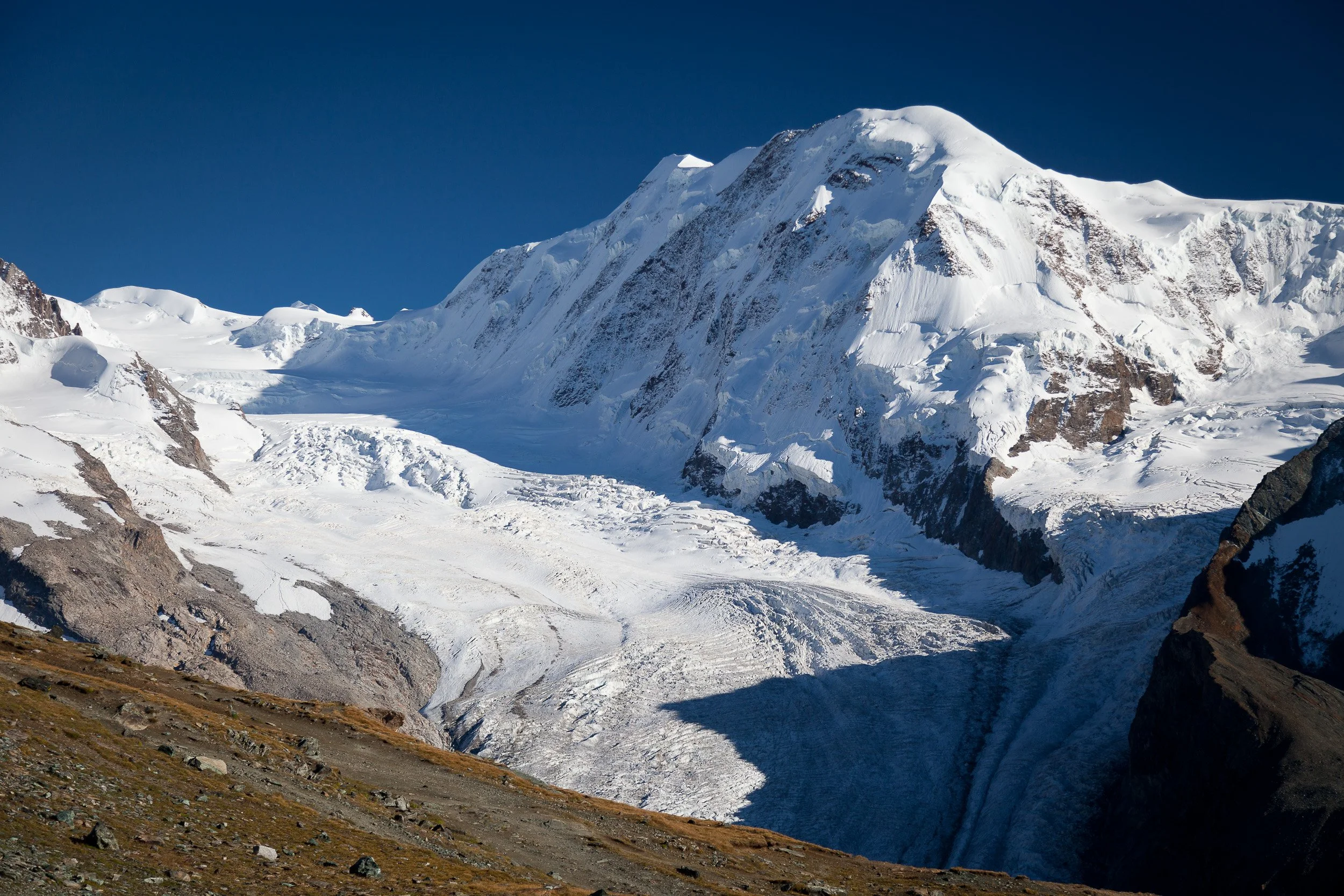 Vast white glacier and high alpine peaks near Gornergrat, streaked with crevasses and framed by a deep blue Swiss sky.