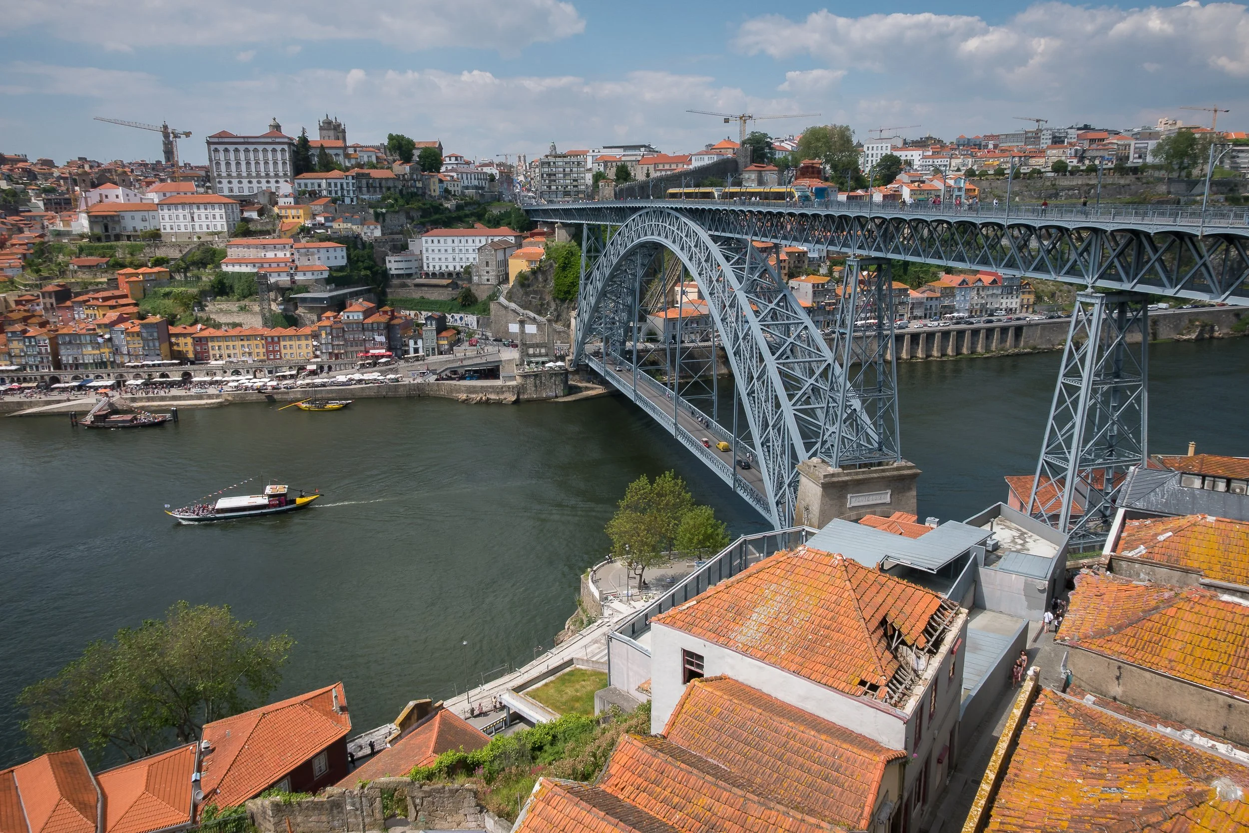 The Dom Luís I Bridge spans the Douro River between Porto and Vila Nova de Gaia, with orange rooftops and river traffic below.
