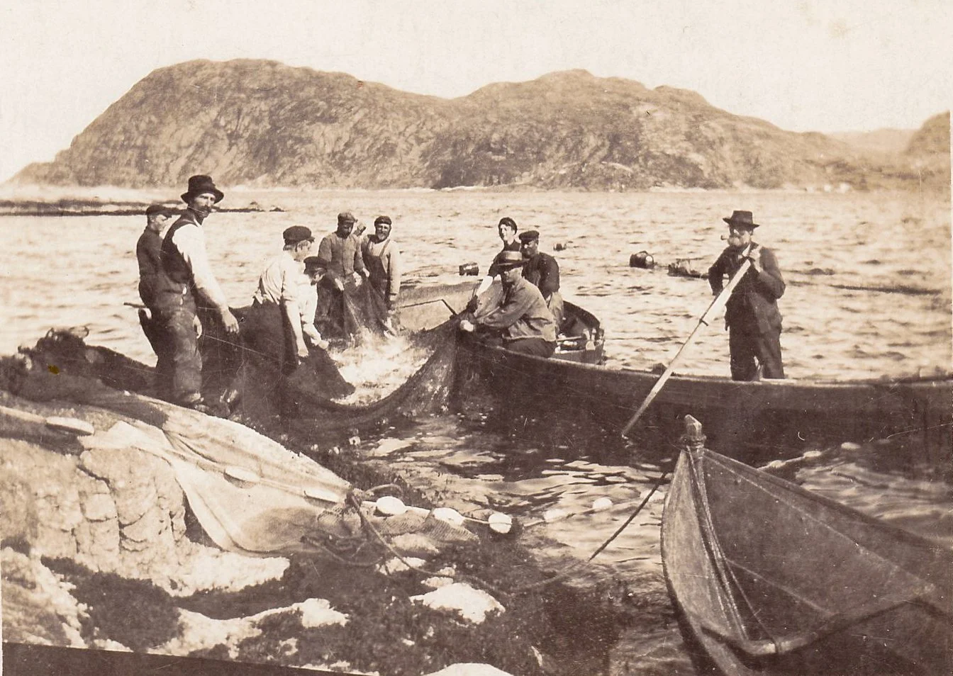 Historisk bilde av makrellsteng i Stranda i Husevåg i august 1922, med fiskere, not og åpne båter ved land.