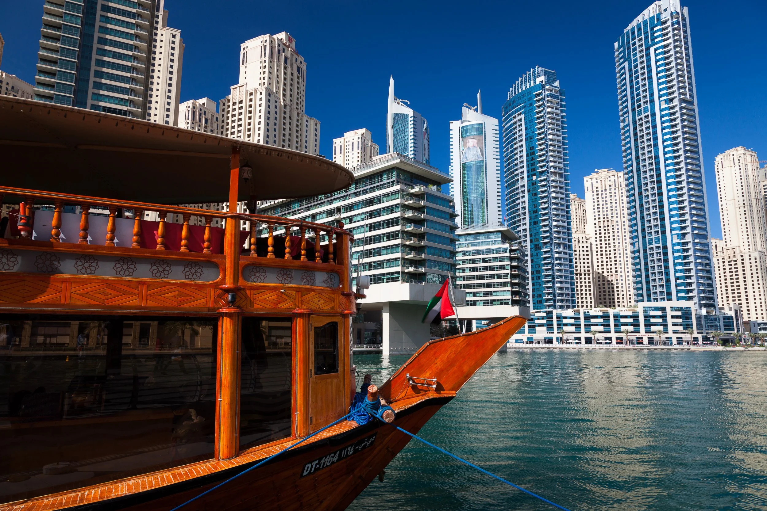 A traditional wooden dhow moored against the glass-and-steel skyline of Dubai Marina.