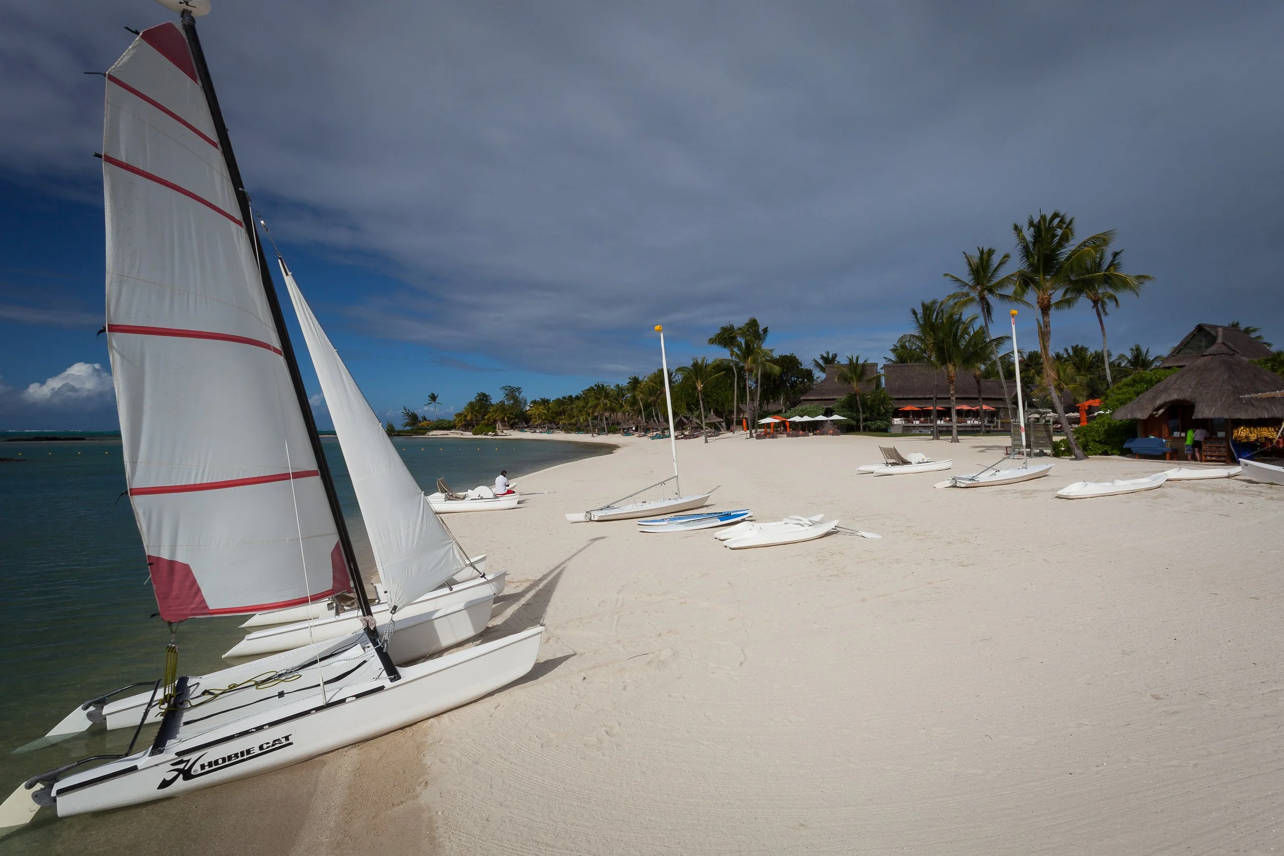Hobie Cat catamarans and small sailboats pulled up on the sand at Constance Le Prince Maurice, ready for a sail on the calm lagoon.
