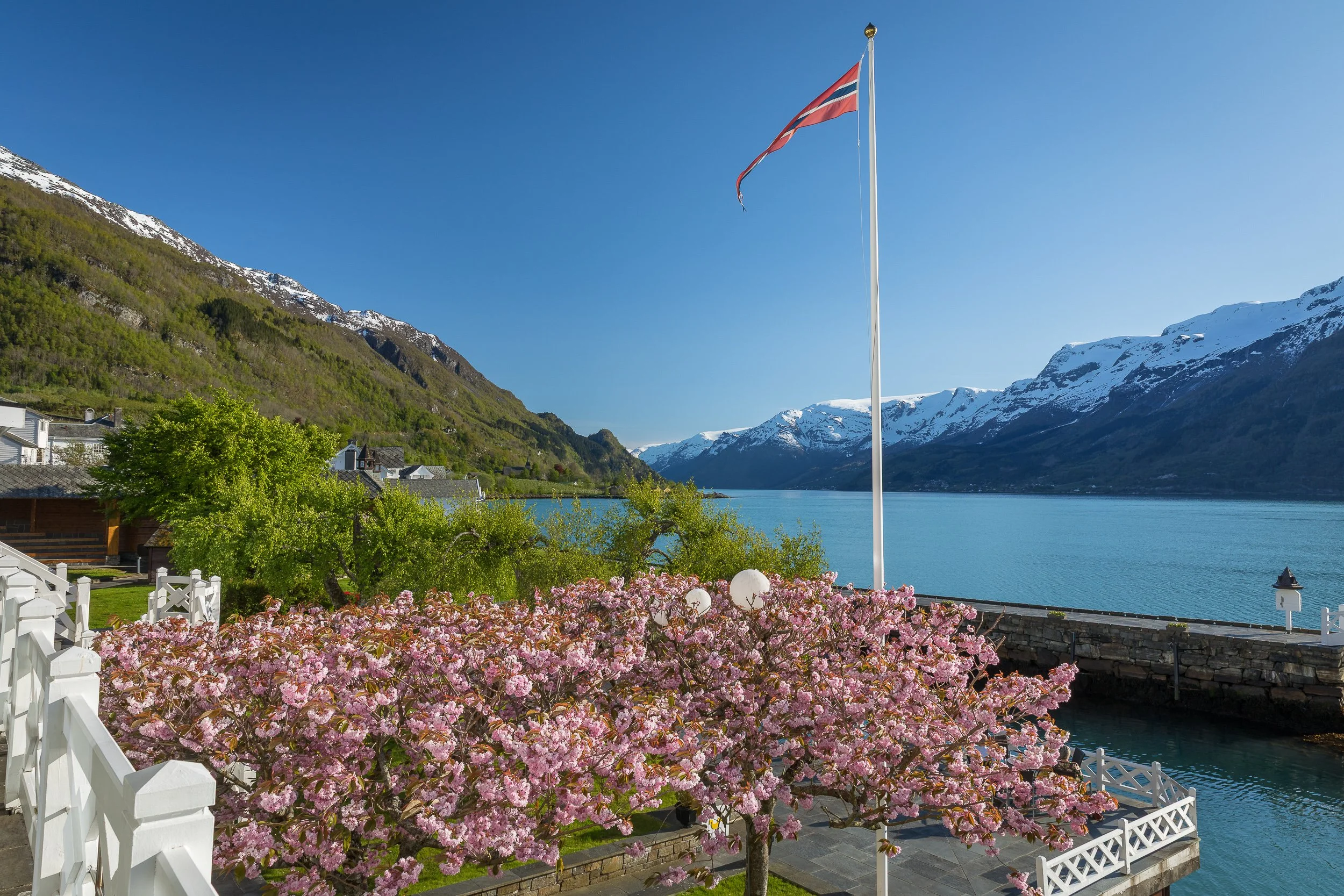 Spring by Hotel Ullensvang in Lofthus, with blossom, the Norwegian flag and the blue Hardangerfjord.