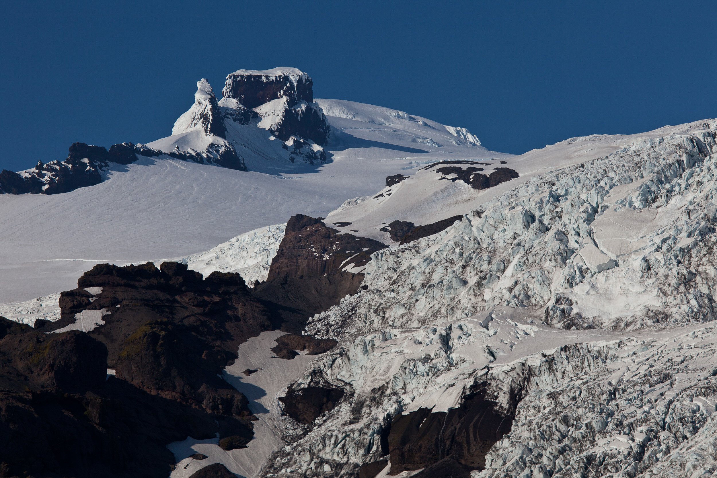 Skaftafell region, Iceland — serrated icefalls and blue crevasses cascade from Vatnajökull, pinned against dark volcanic ridges.
