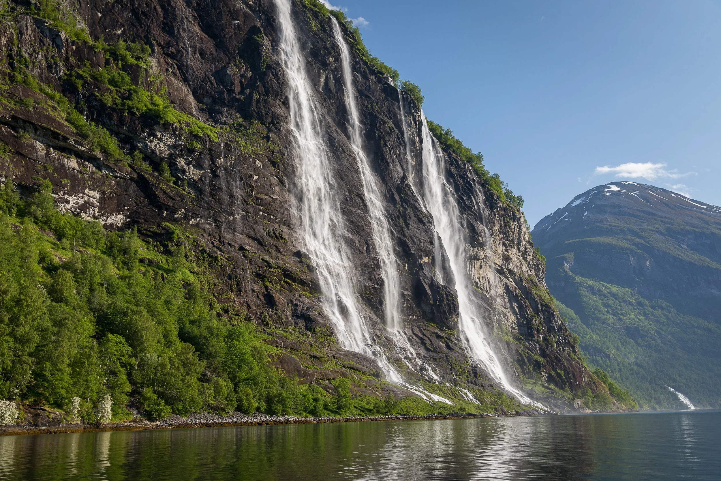 Seven Sisters in Geirangerfjorden again — a wider fjord view where waterfalls, cliffs and calm water collide in pure spectacle.