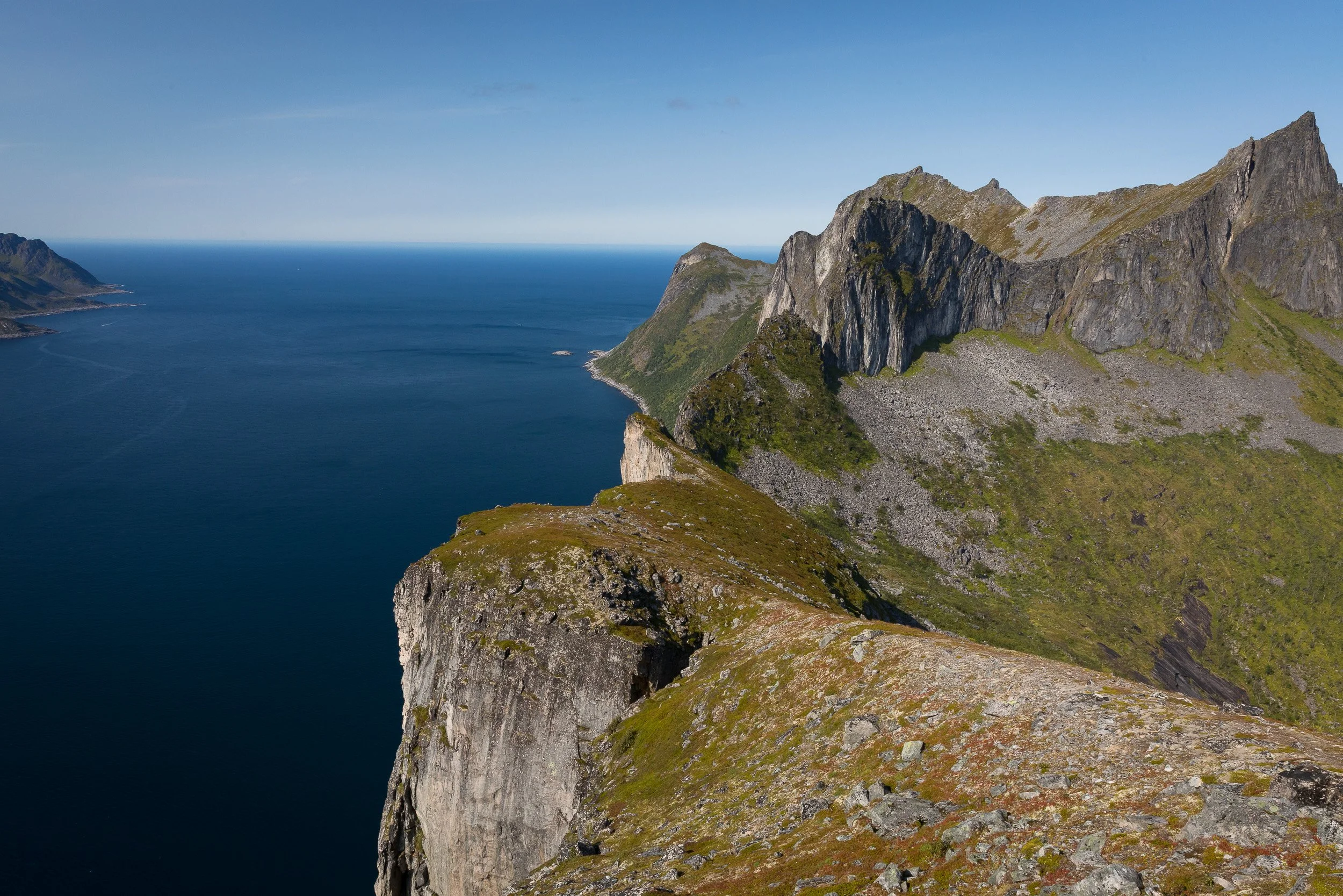 A high view from Hesten across rugged ridges and the open sea, with grey rock, green slopes and clear Arctic light shaping the scene.