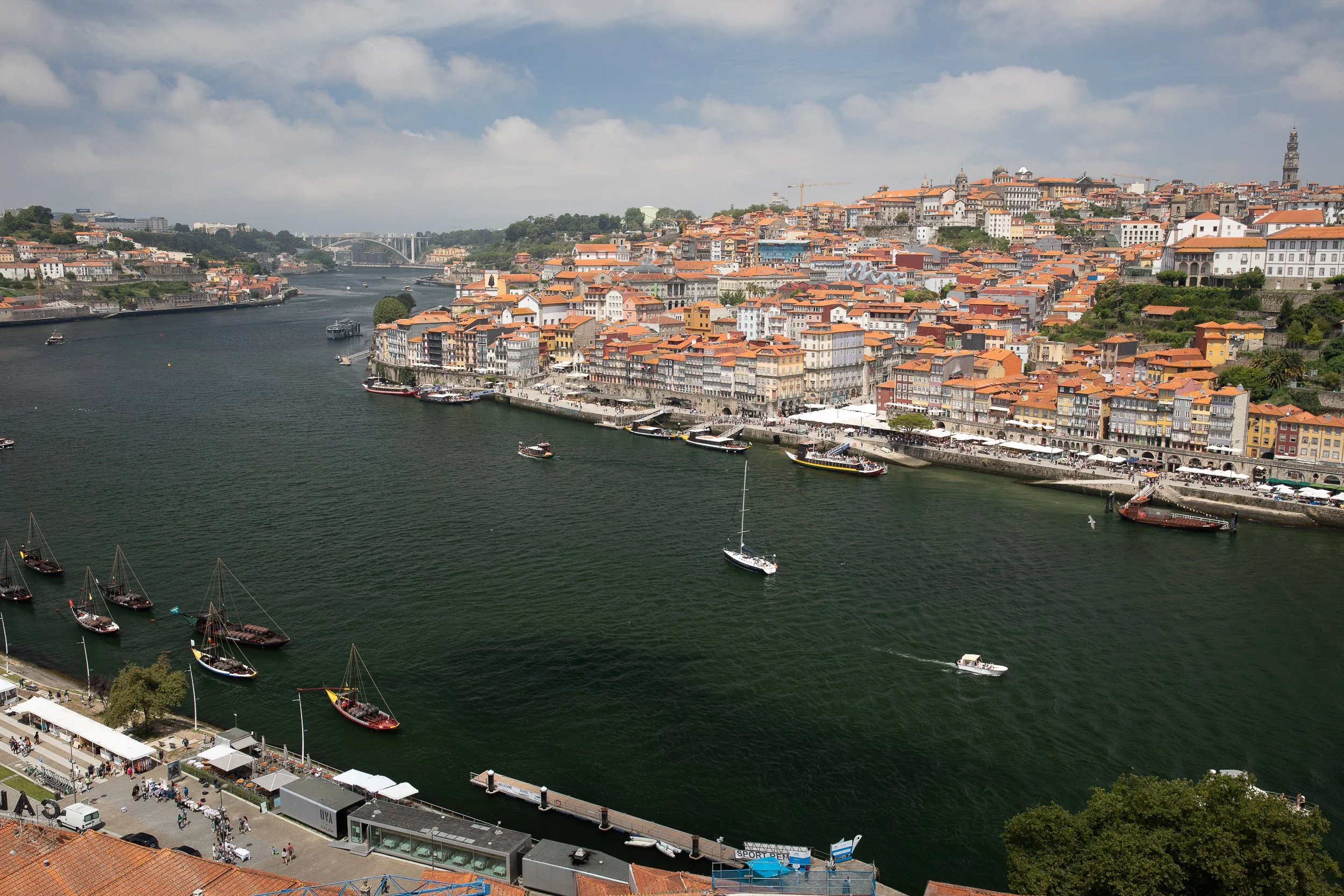Porto’s Ribeira waterfront seen across the Douro River, with rabelo boats, orange rooftops and the historic city rising above the quay.
