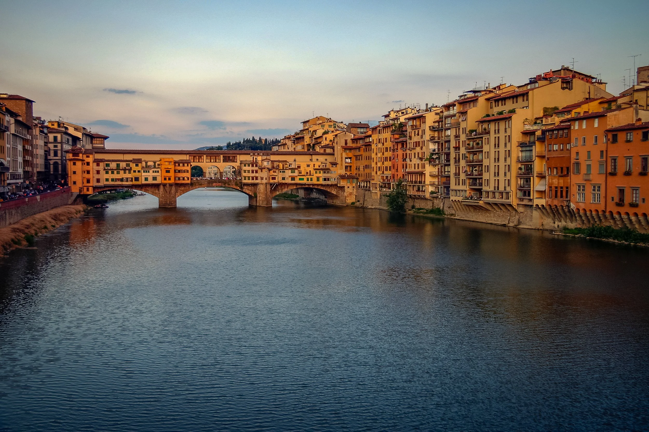 Ponte Vecchio at dusk, with the warm façades of Florence reflected in the slow waters of the Arno.