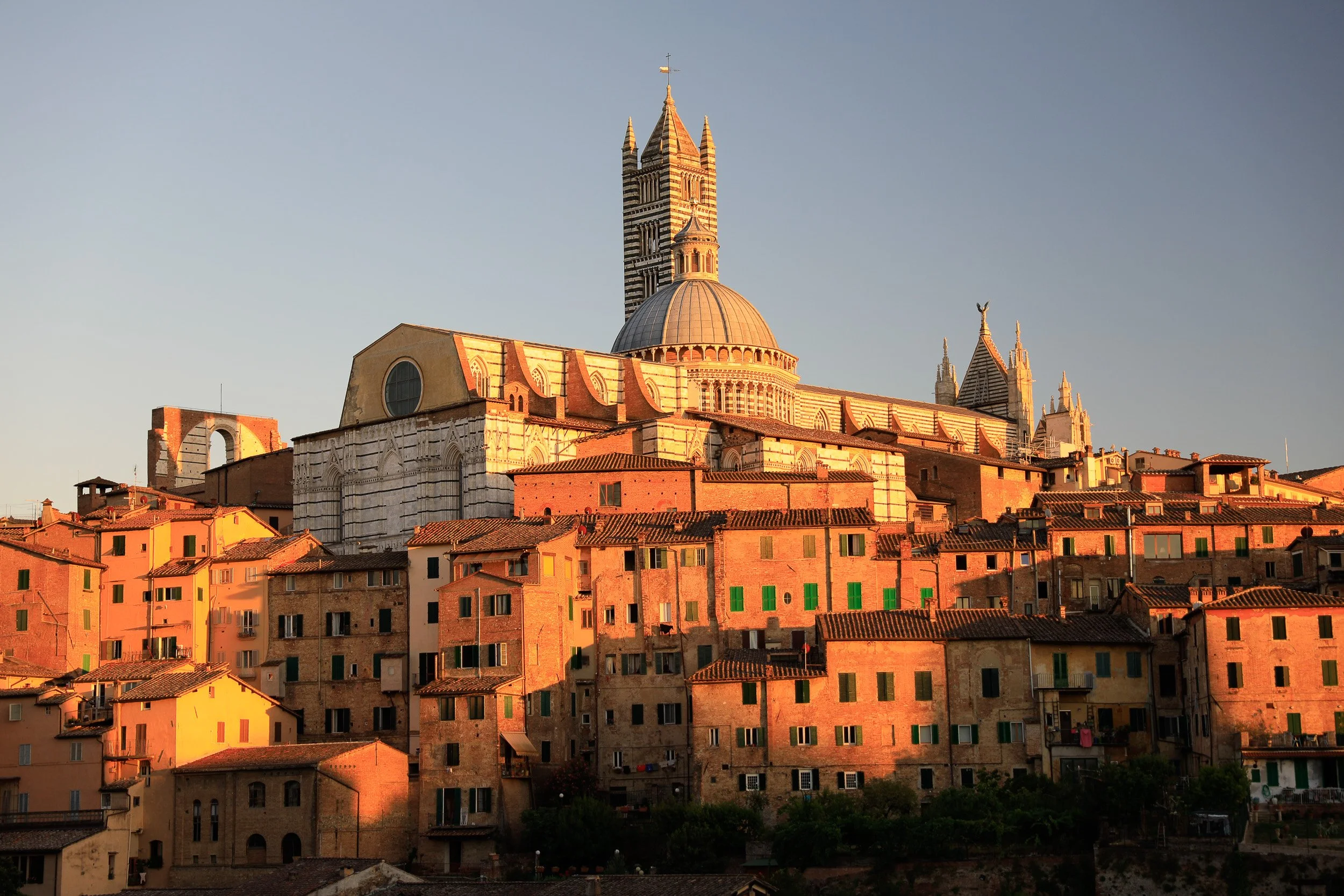Siena Cathedral rising above terracotta roofs, caught in the last warm light of evening.