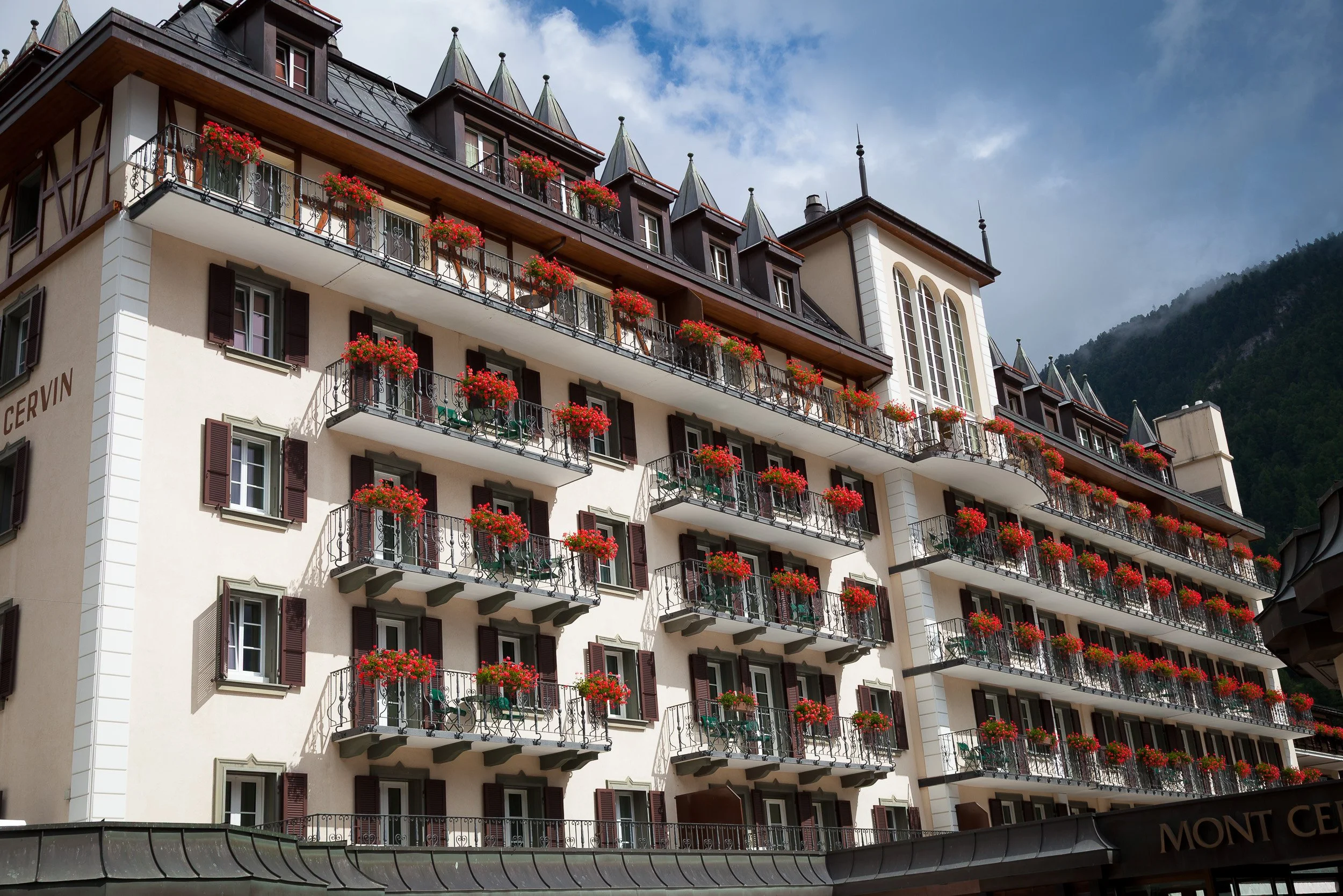 Elegant façade of the historic Mont Cervin hotel in Zermatt, every balcony lined with vivid red flower boxes.