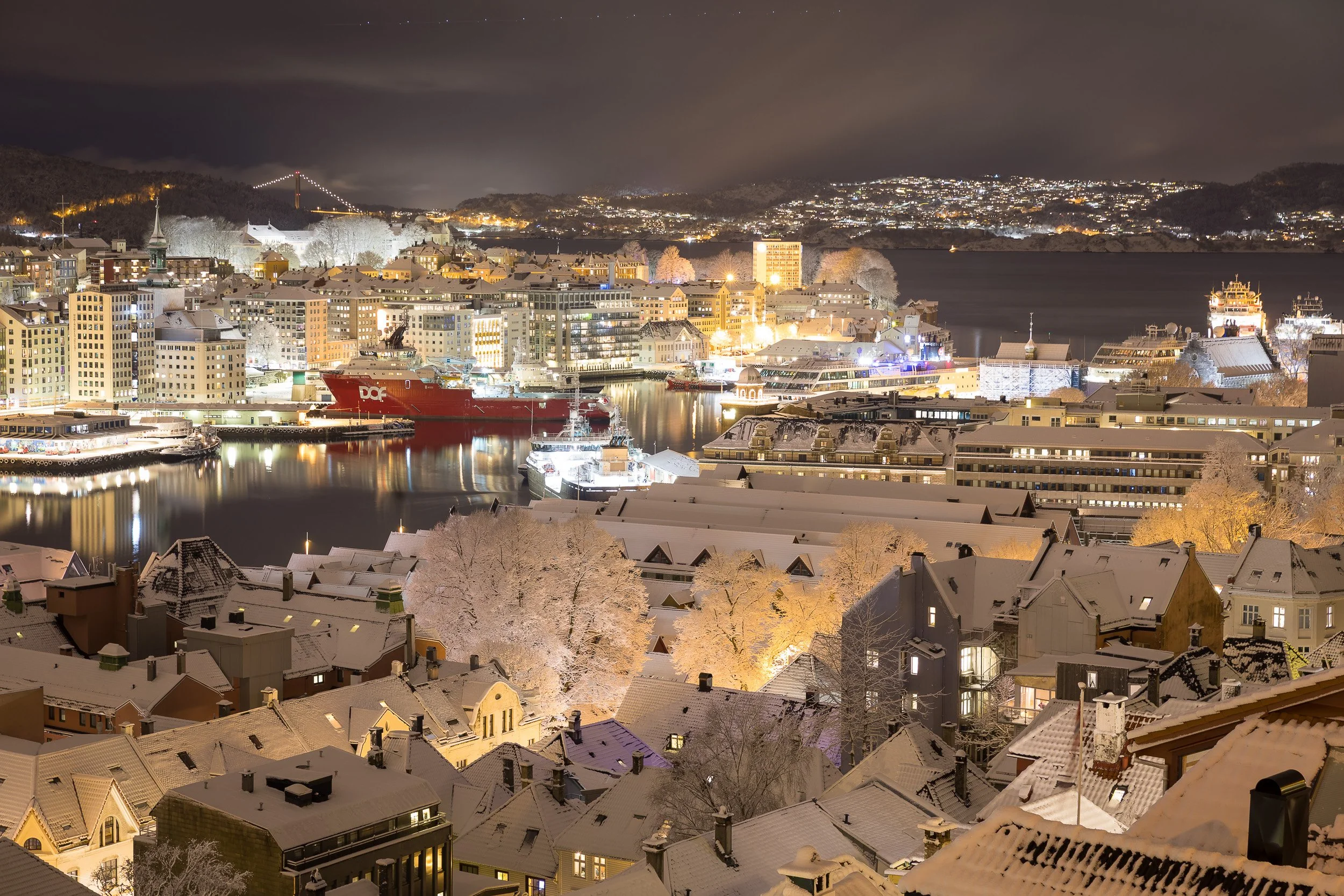 Bergen harbor in winter—city lights glowing across snow and sea, Norway