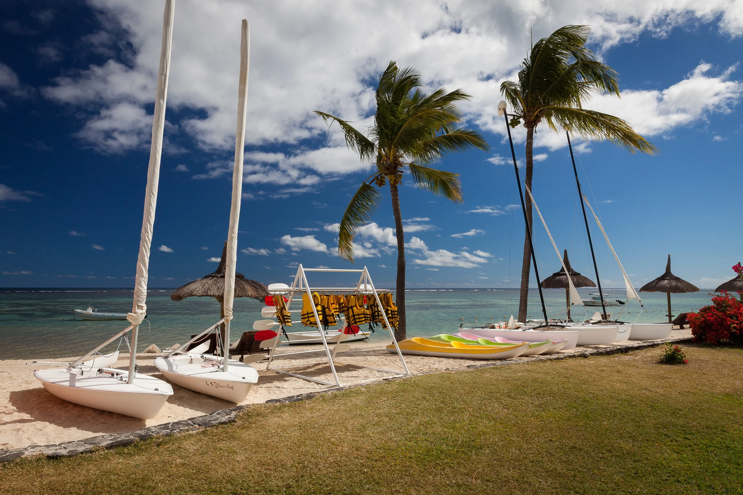 Water sports set-up on Flic en Flac beach, Mauritius, with dinghies, kayaks and life jackets lined up beside the turquoise lagoon and swaying palms.