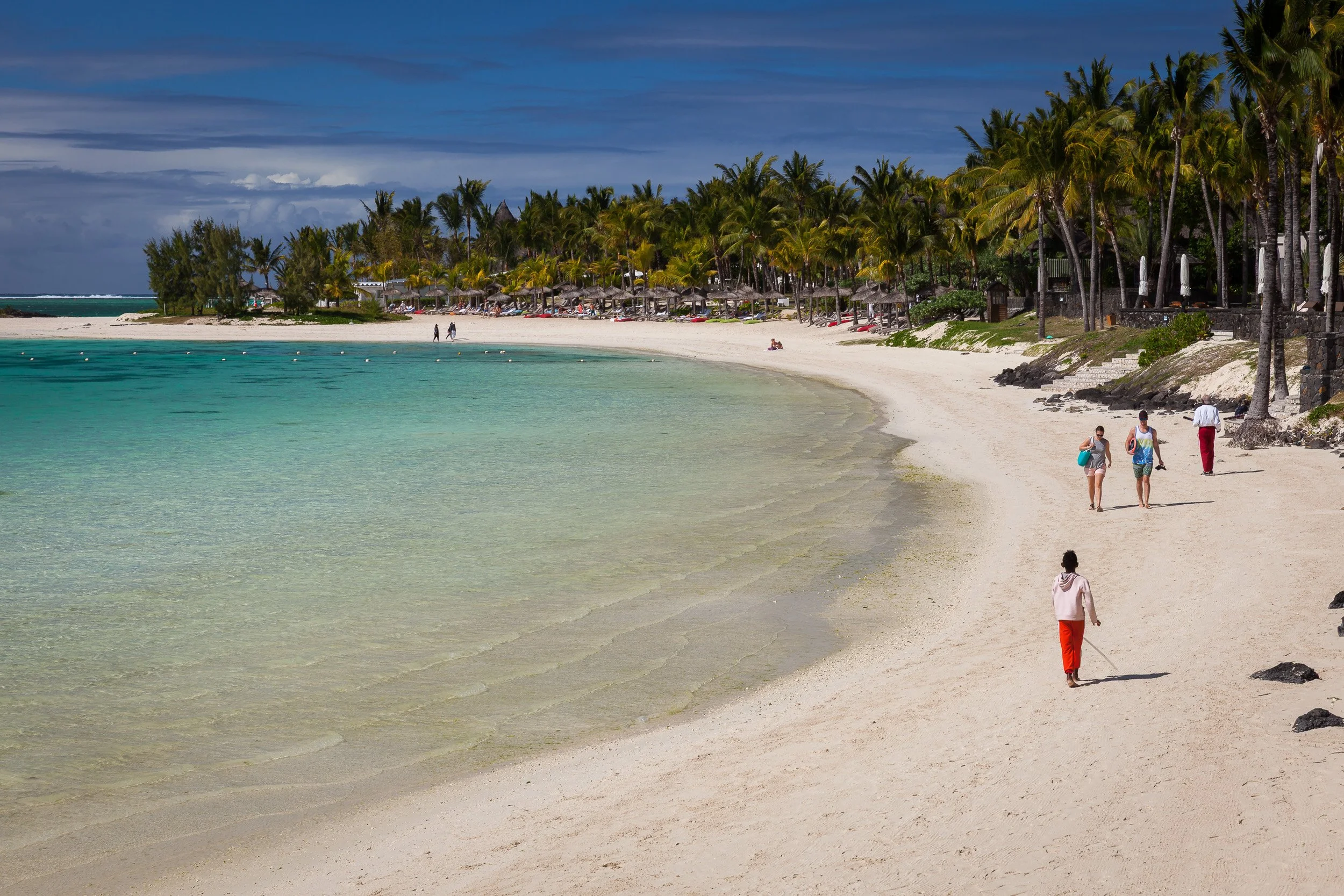 Holidaymakers wandering along the shoreline at Belle Mare Beach, enjoying the warm shallows and palm-fringed sand.