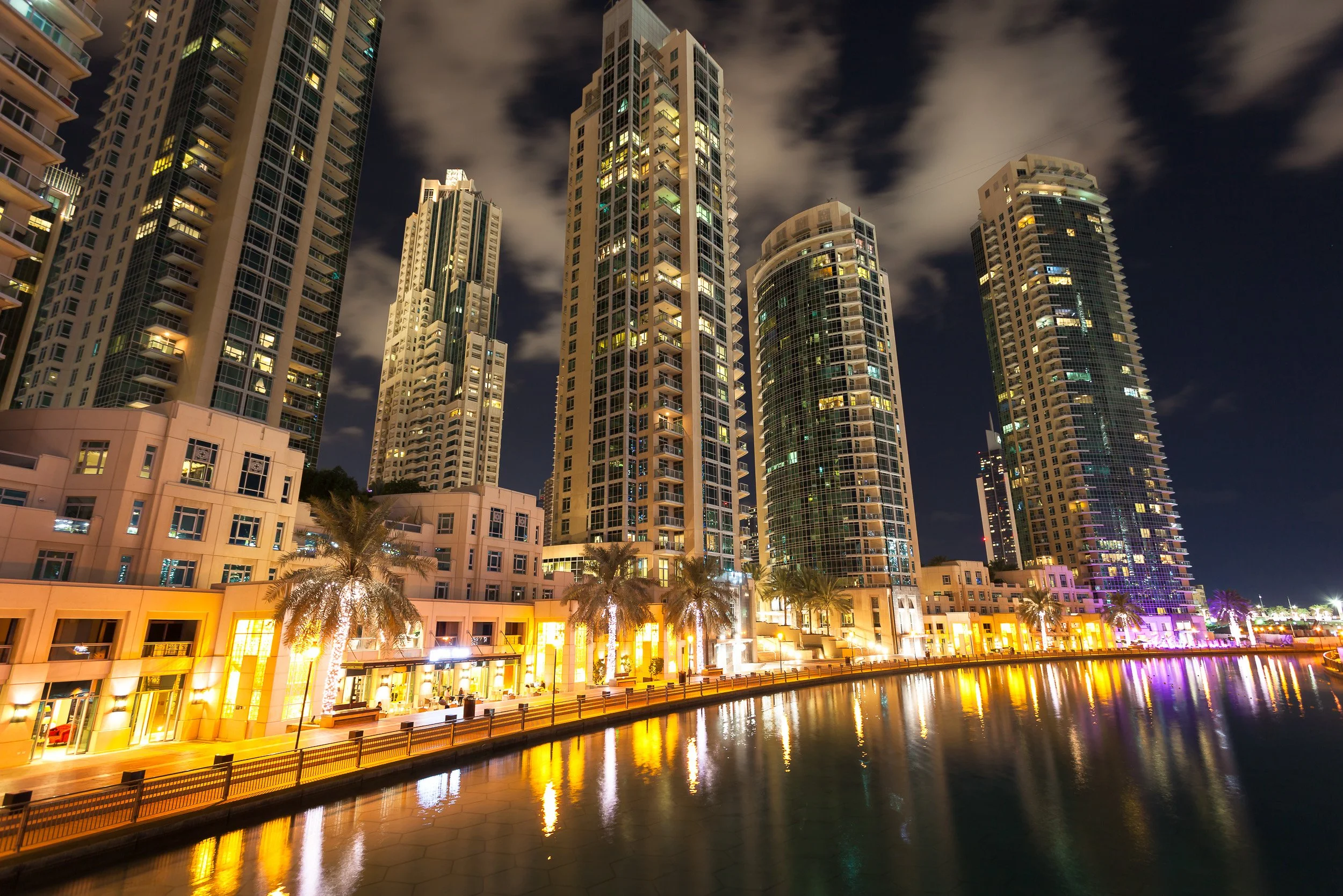 Dubai Marina’s residential towers glowing above still water on a warm evening.