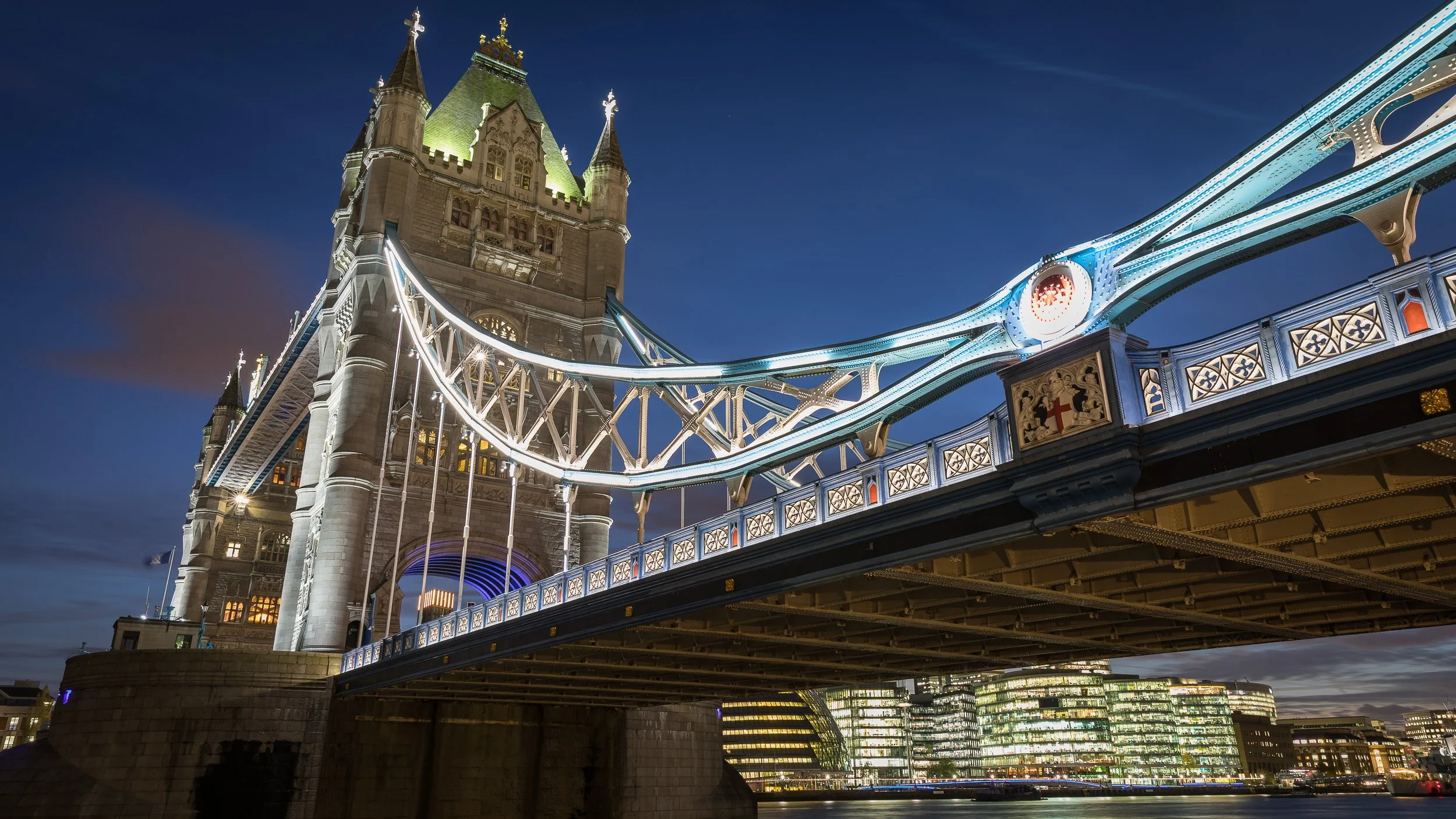 Tower Bridge at blue hour in London, UK – illuminated steelwork, stone towers and city lights above the River Thames.