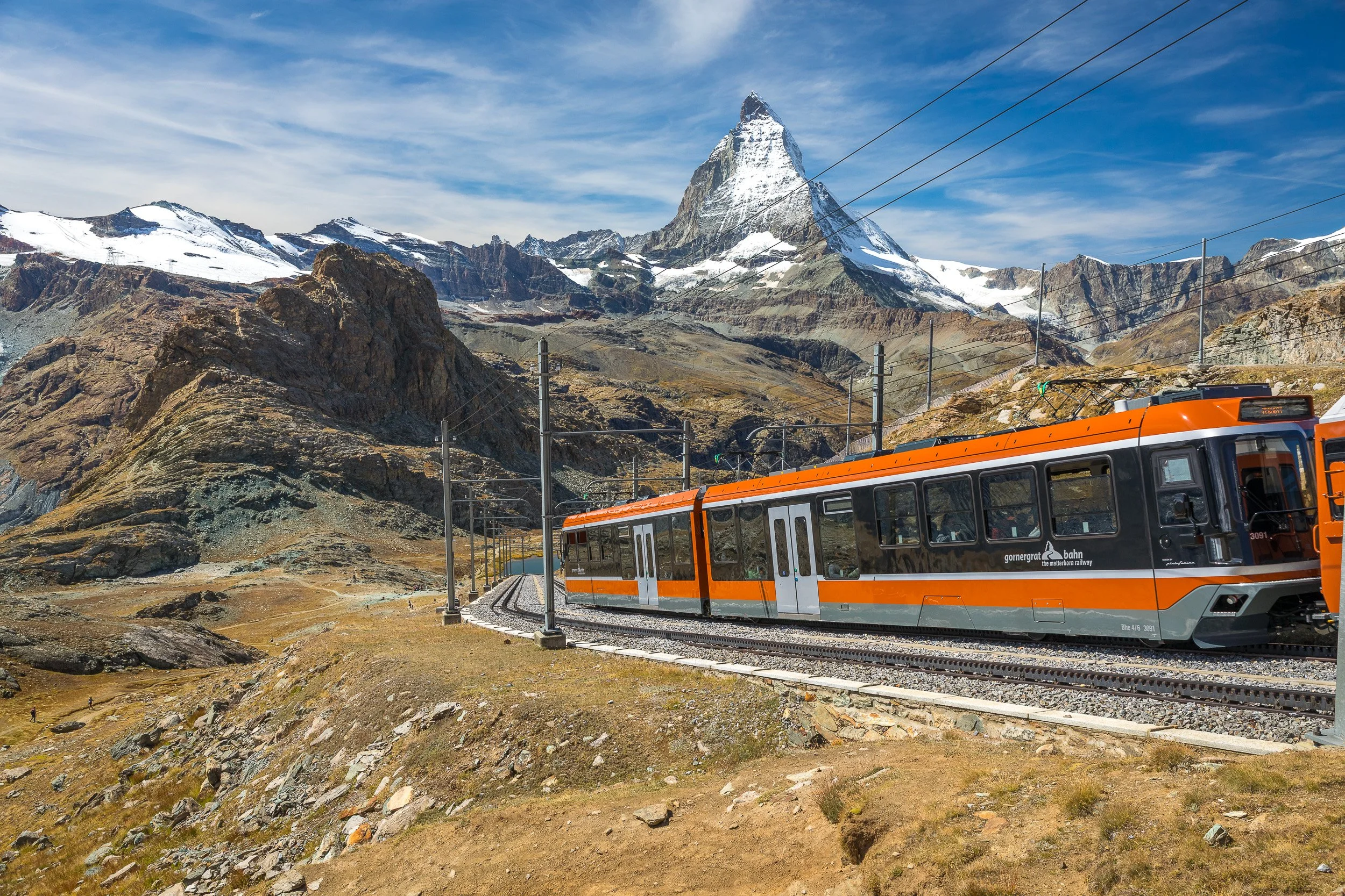 Modern Gornergrat train curving along high mountain tracks with the Matterhorn and rocky ridges behind.