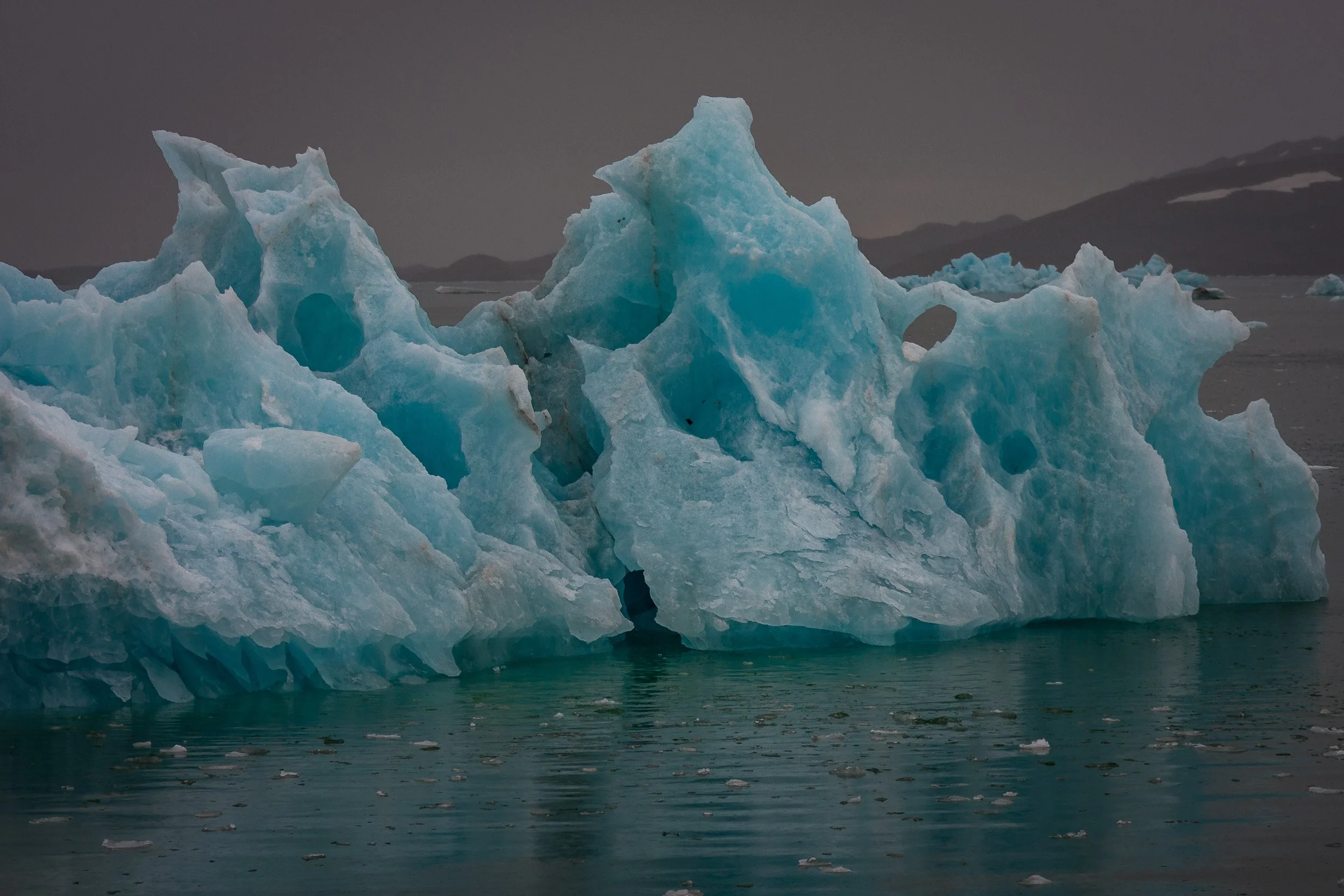 This fractured iceberg glows with dense blue tones, its carved openings giving the ice an almost architectural form.