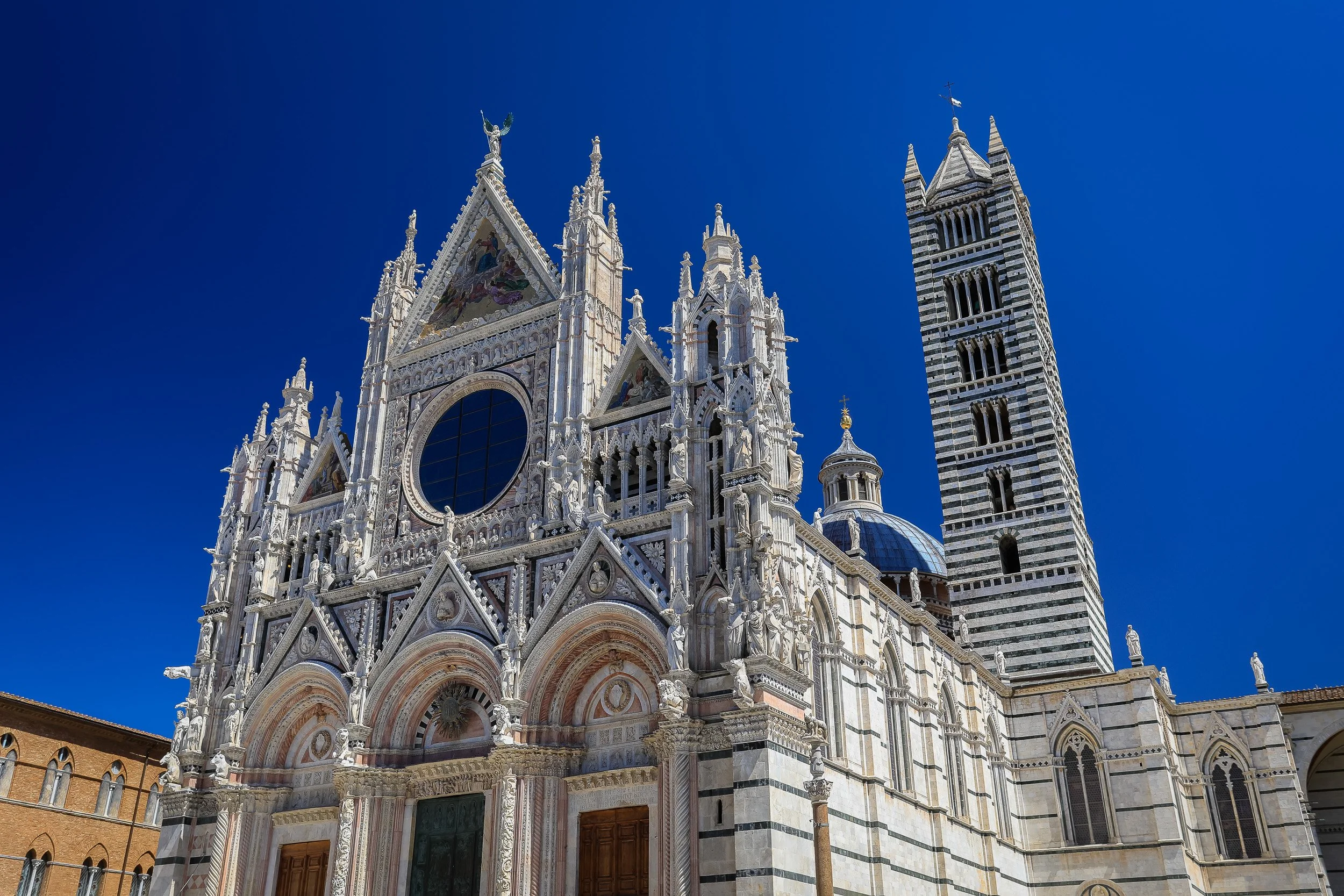 The sculpted façade of Siena Cathedral beneath a deep blue sky, bright white marble set against the summer light.