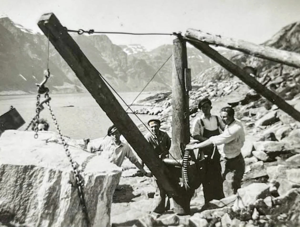 Historisk svart-hvittbilde fra steinbruddet i Krabbestig på Husevågøy, der flere menn bruker kjetting og en enkel løfteordning til å håndtere en stor steinblokk ved Fåfjorden.