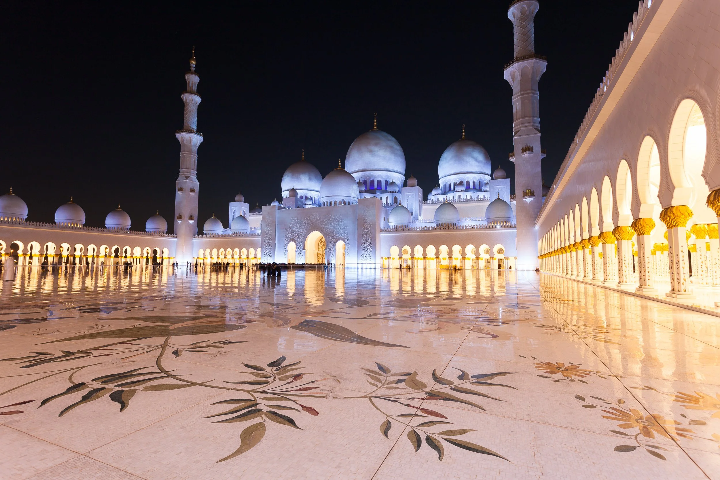 The marble courtyard of Sheikh Zayed Grand Mosque shining under the night sky, Abu Dhabi.