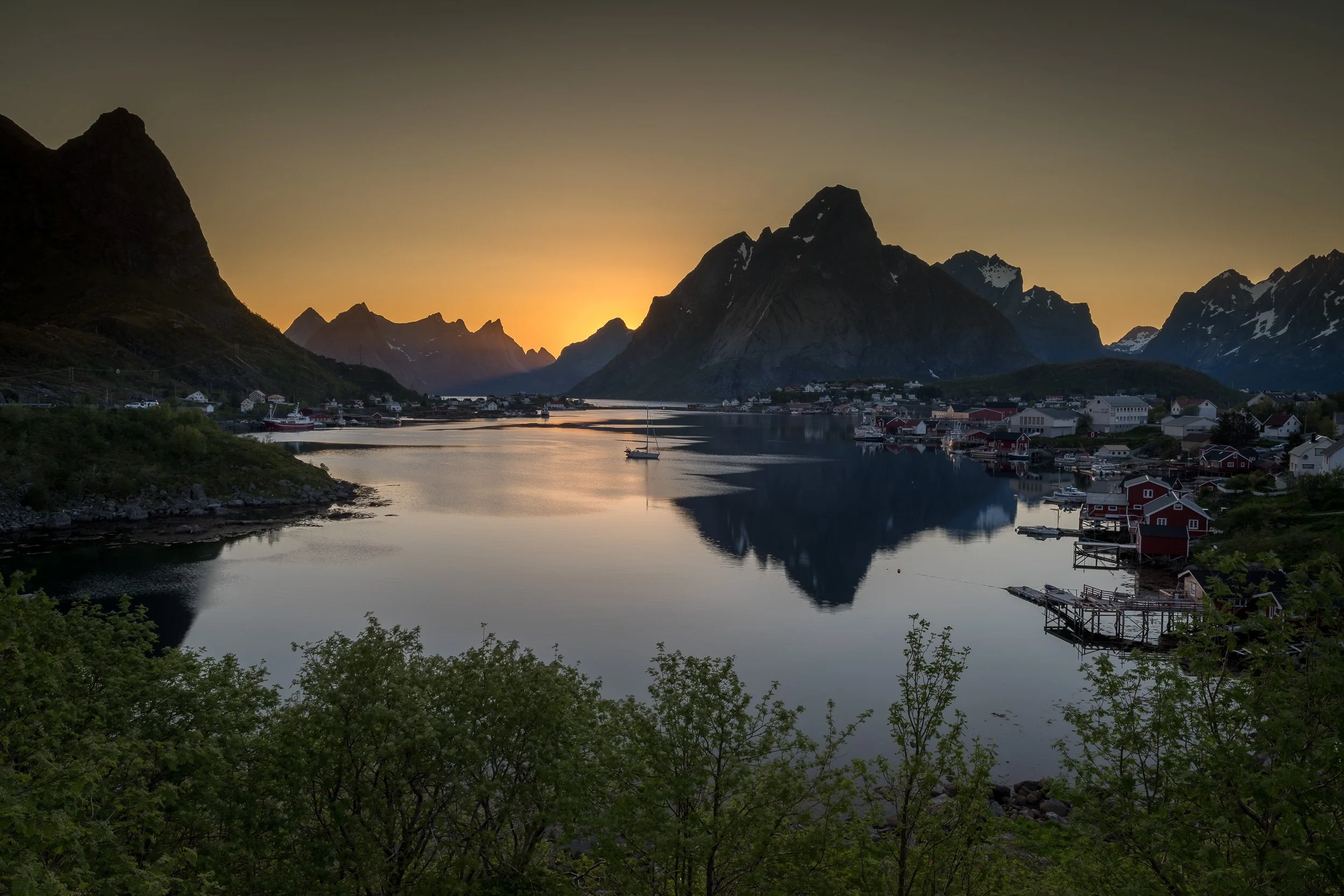 Midnight sun in Reine, Lofoten Islands, Norway – low Arctic sun glowing over the fjord and mountain peaks at night.