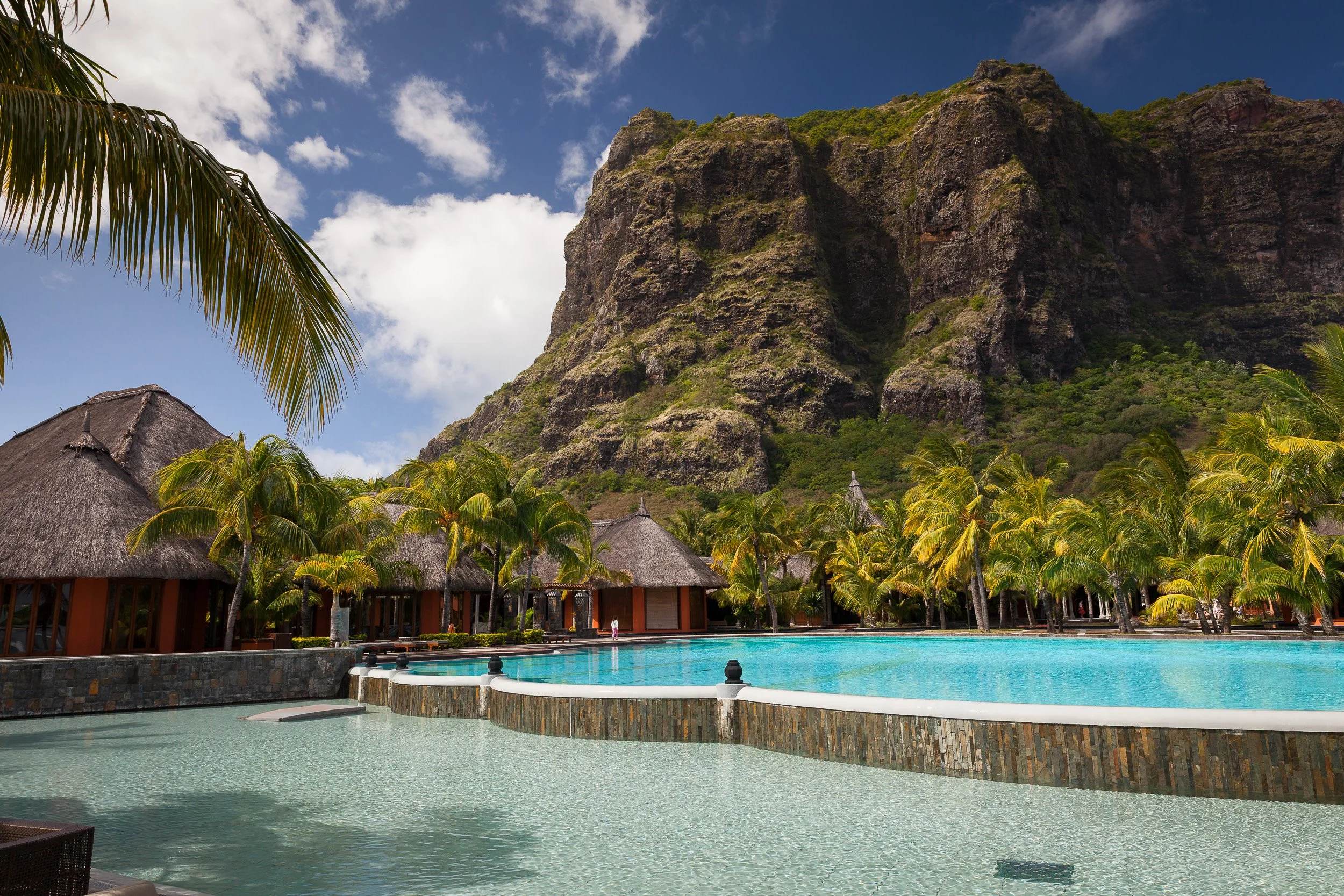 Infinity pool at a Le Morne beach resort in Mauritius, backed by towering Le Morne Brabant and fringed with palm-roofed villas.