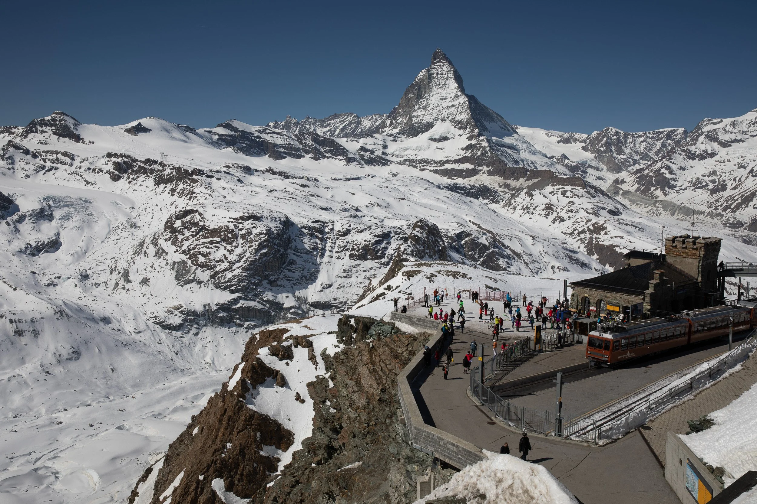 Winter panorama from Gornergrat, with skiers on the viewing terrace, the cogwheel train and the Matterhorn dominating the skyline.