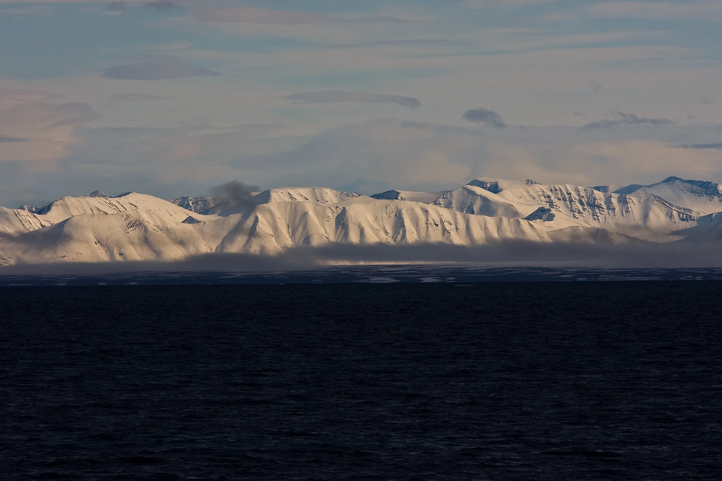 At 80 degrees north, light falls across a distant mountain wall above dark polar water.