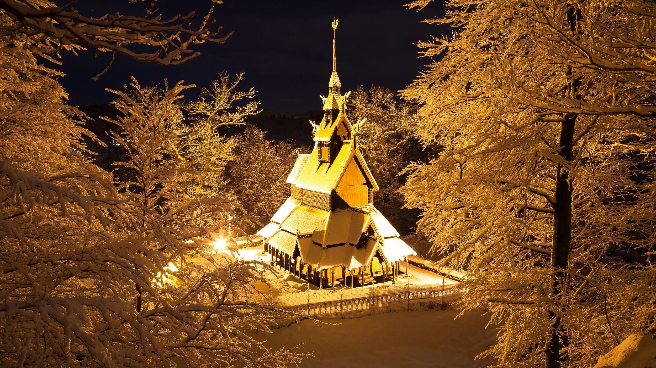 Fantoft Stave Church in Bergen, Norway – historic wooden church softly lit against the dark evening forest.
