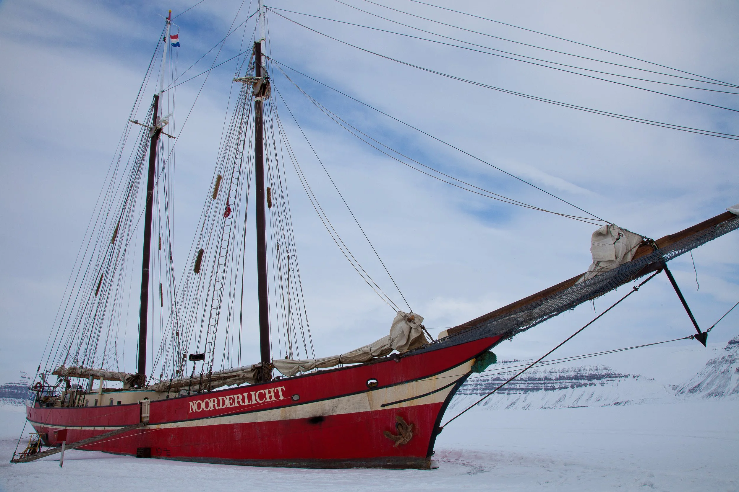 The schooner Noorderlicht lies frozen into the ice, a striking reminder of travel and endurance in Svalbard winter.