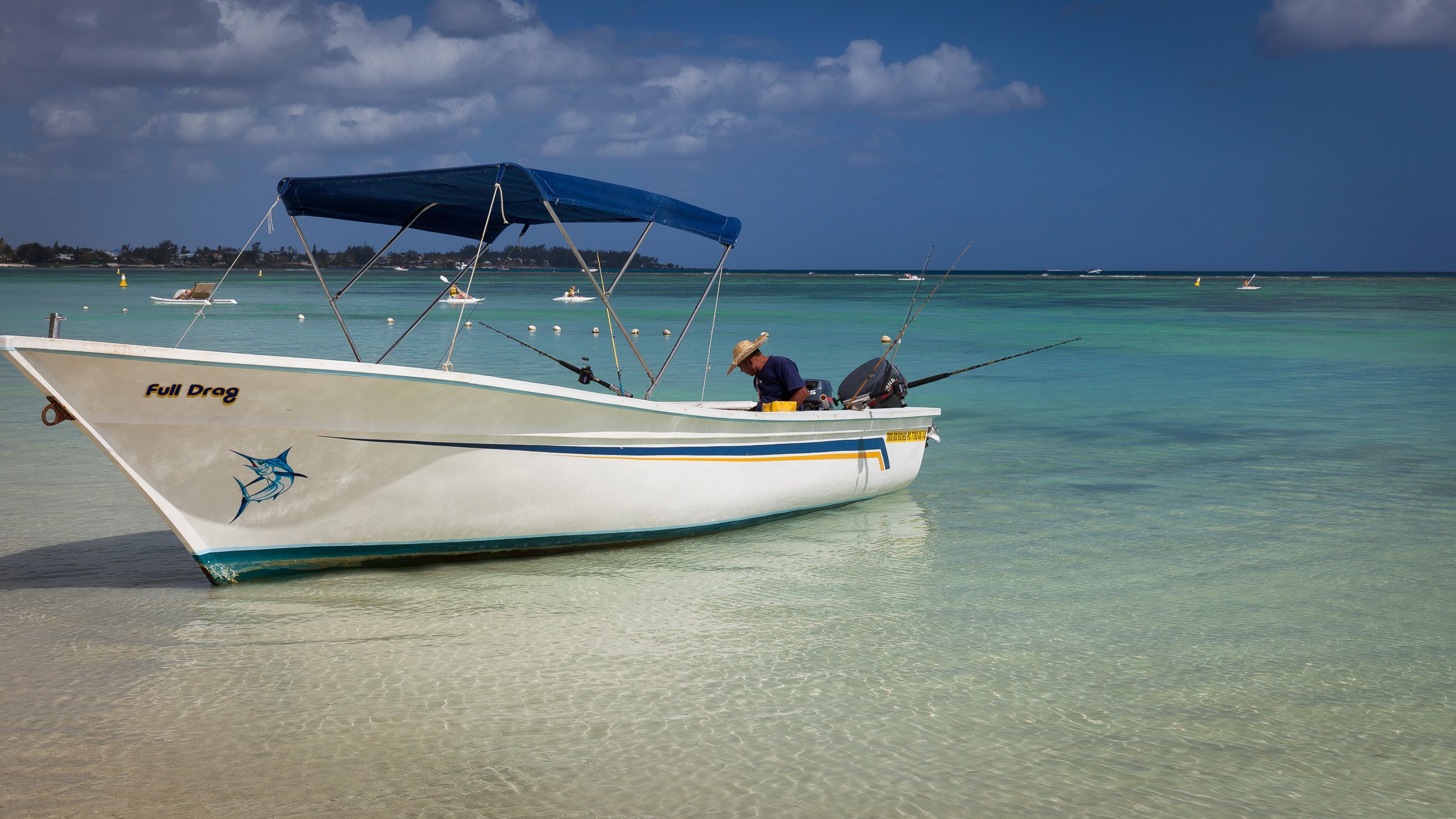 Fisherman in a small boat at Trou aux Biches, Grand Baie, calmly preparing his gear beside a wooden jetty on the turquoise lagoon