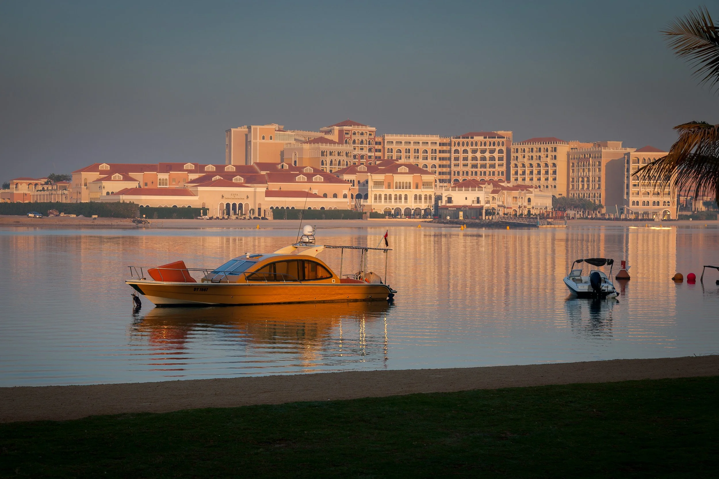 Still morning water, anchored boats and soft pastel light along the Abu Dhabi shore.