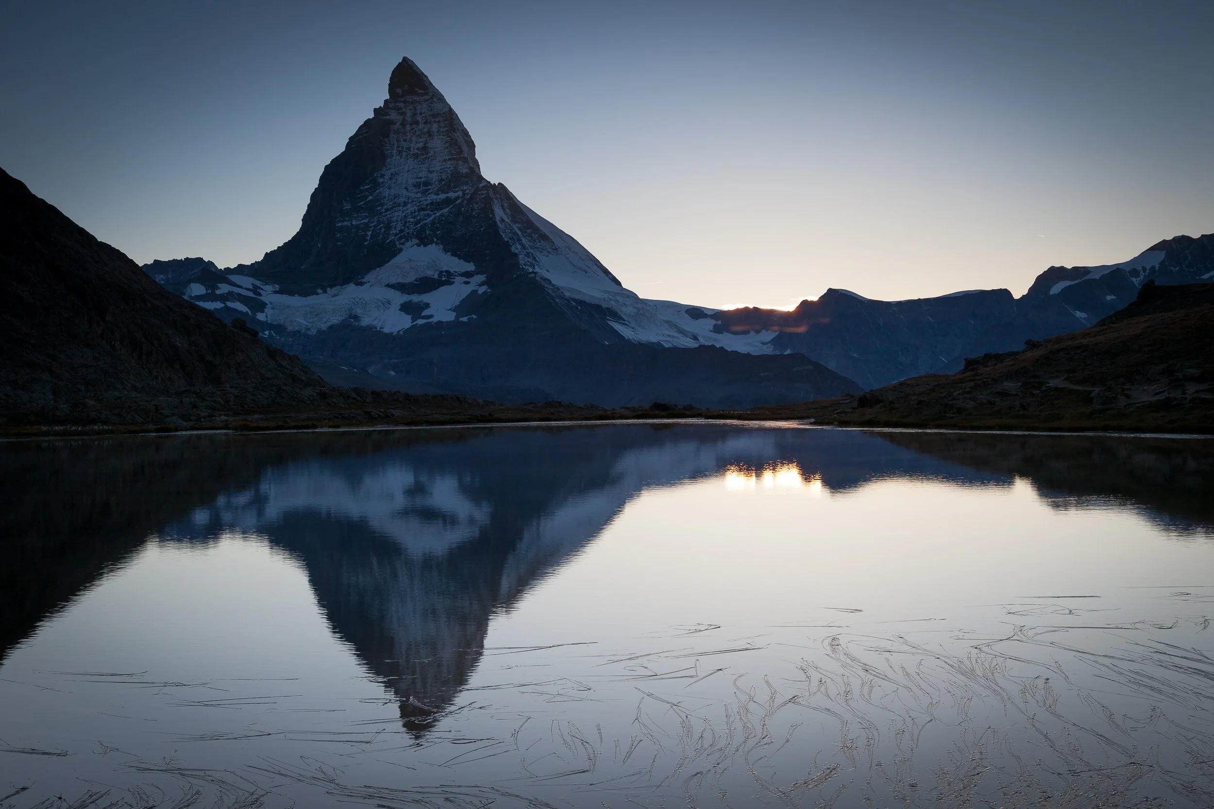 Silhouette of the Matterhorn and its reflection in still Riffelsee at dusk, with the last glow of light along the horizon.