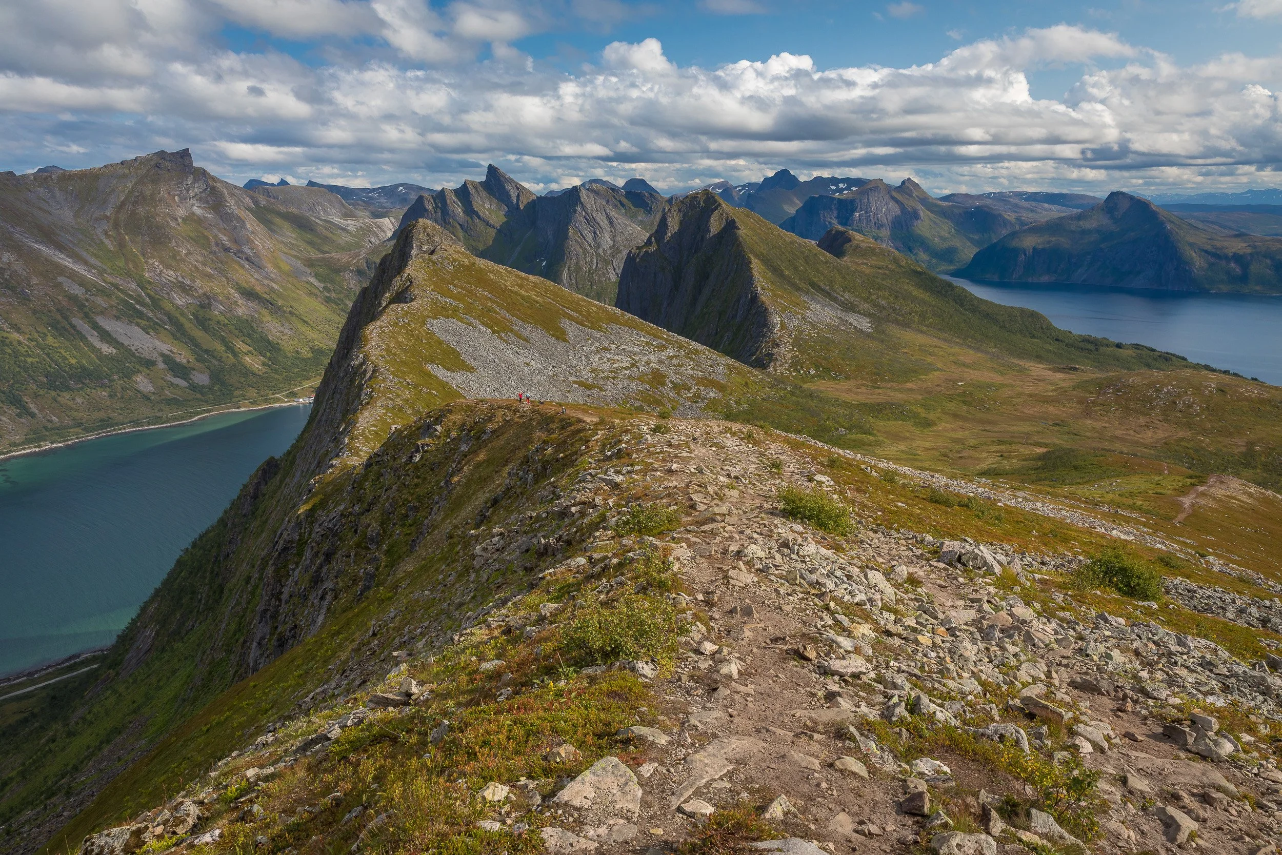 The trail from Husfjellet follows a narrow mountain ridge through a dramatic landscape of peaks, fjords and broken summer cloud.