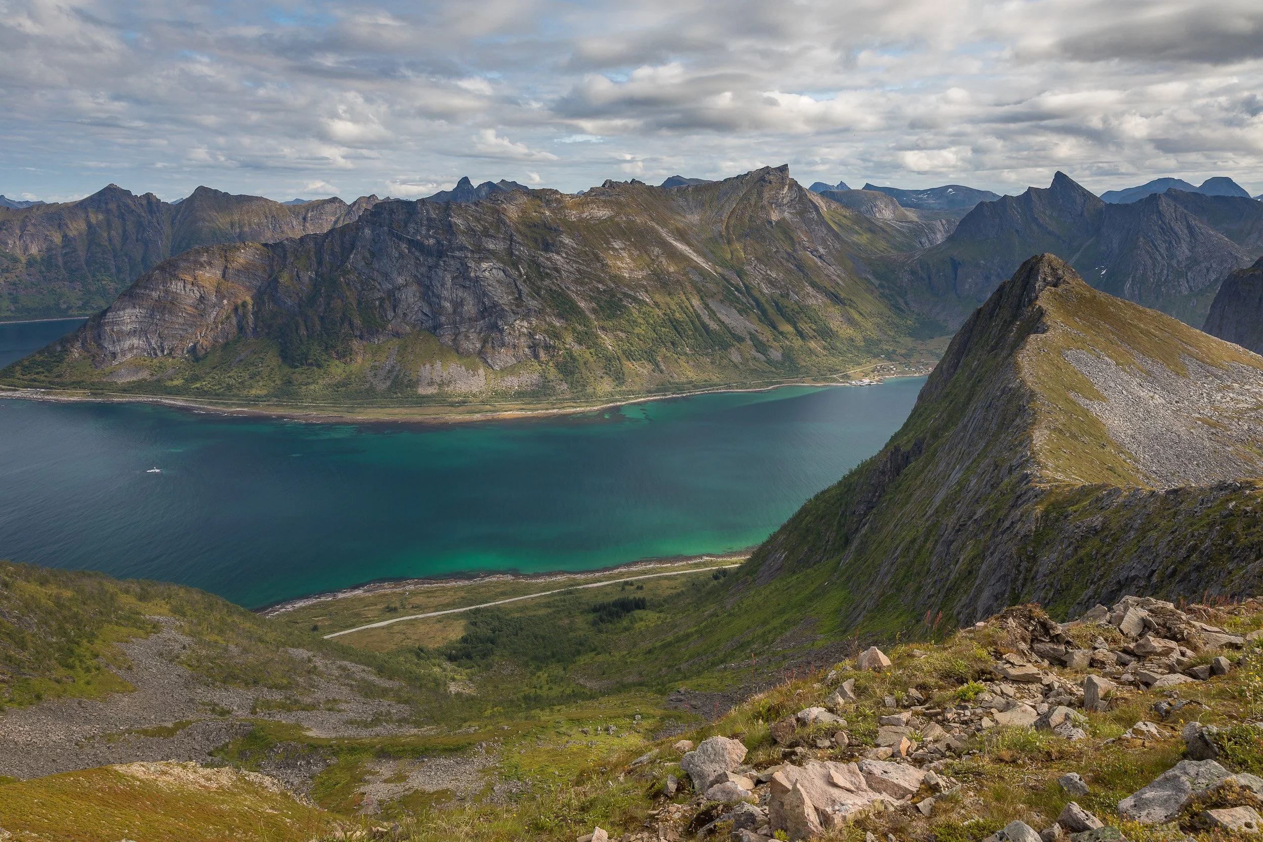 A broad view from Husfjellet across ridges, fjord water and scattered mountain light, showing the layered scale of Senja’s coastal landscape.
